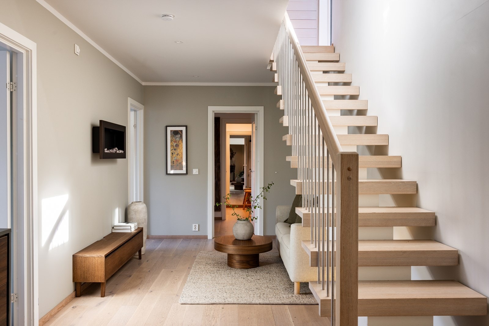 En skyvedør med glassfelt leder inn i en luftig hall med god størrelse, enstavs parkettgulv, downlights og en stilig trapp opp til første etasje. Alle innerdørene er av merket Trend og trappen har midstilt vange, som gir nærmest flytende eiketrinn. Galleribilde