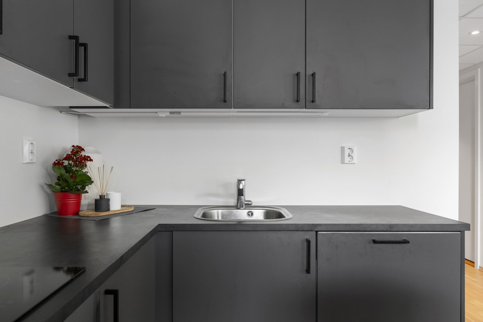 Stilrent og moderne kjøkken med mørkegrå fronter, integrert vask og god oppbevaringsplass. Hvite vegger og dekorative detaljer gir et lunt og innbydende preg. Galleribilde