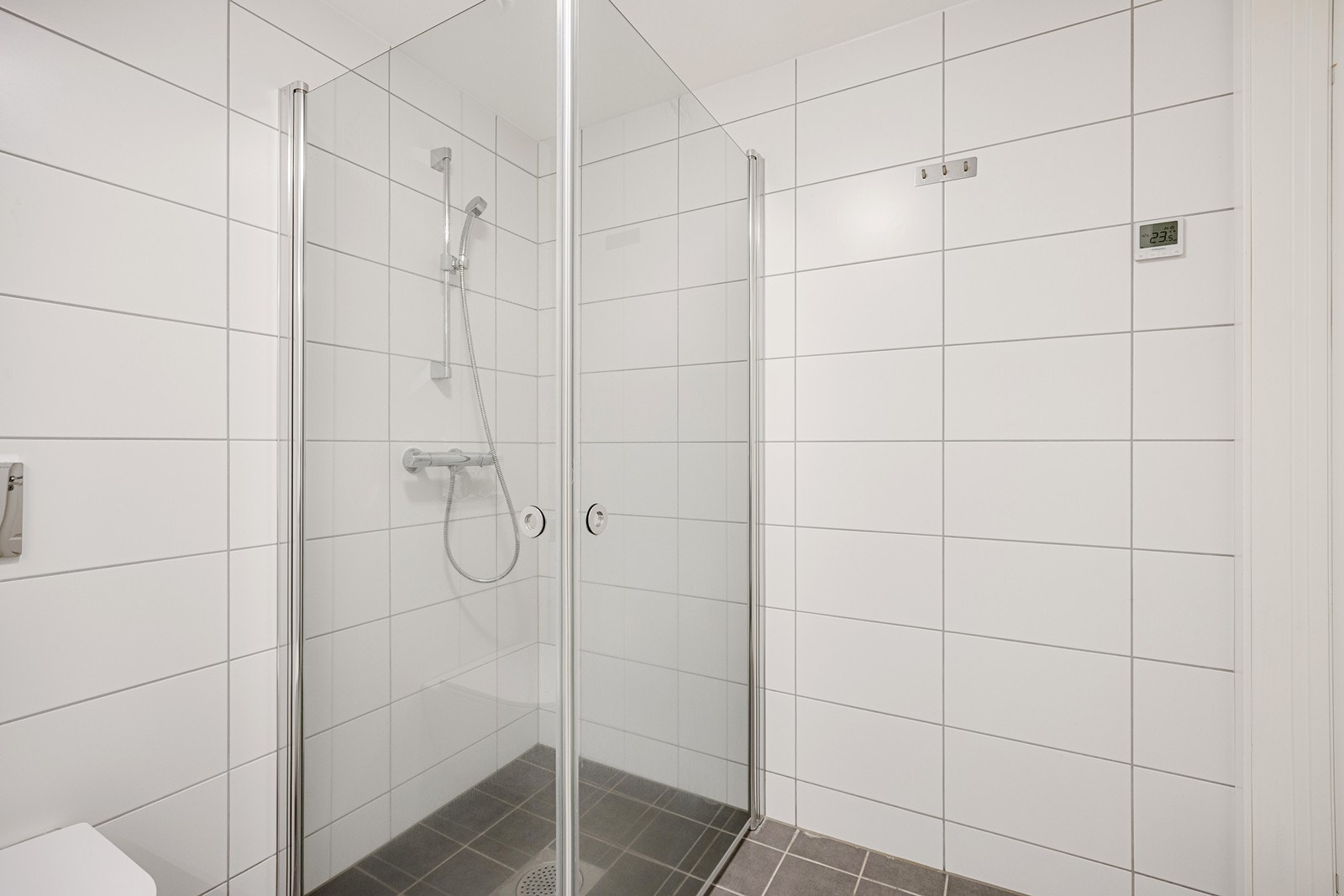 Videre er badet utstyrt med et vegghengt toalett, opplegg for vaskemaskin og et dusjhjørne med innfellbare glassdører Galleribilde