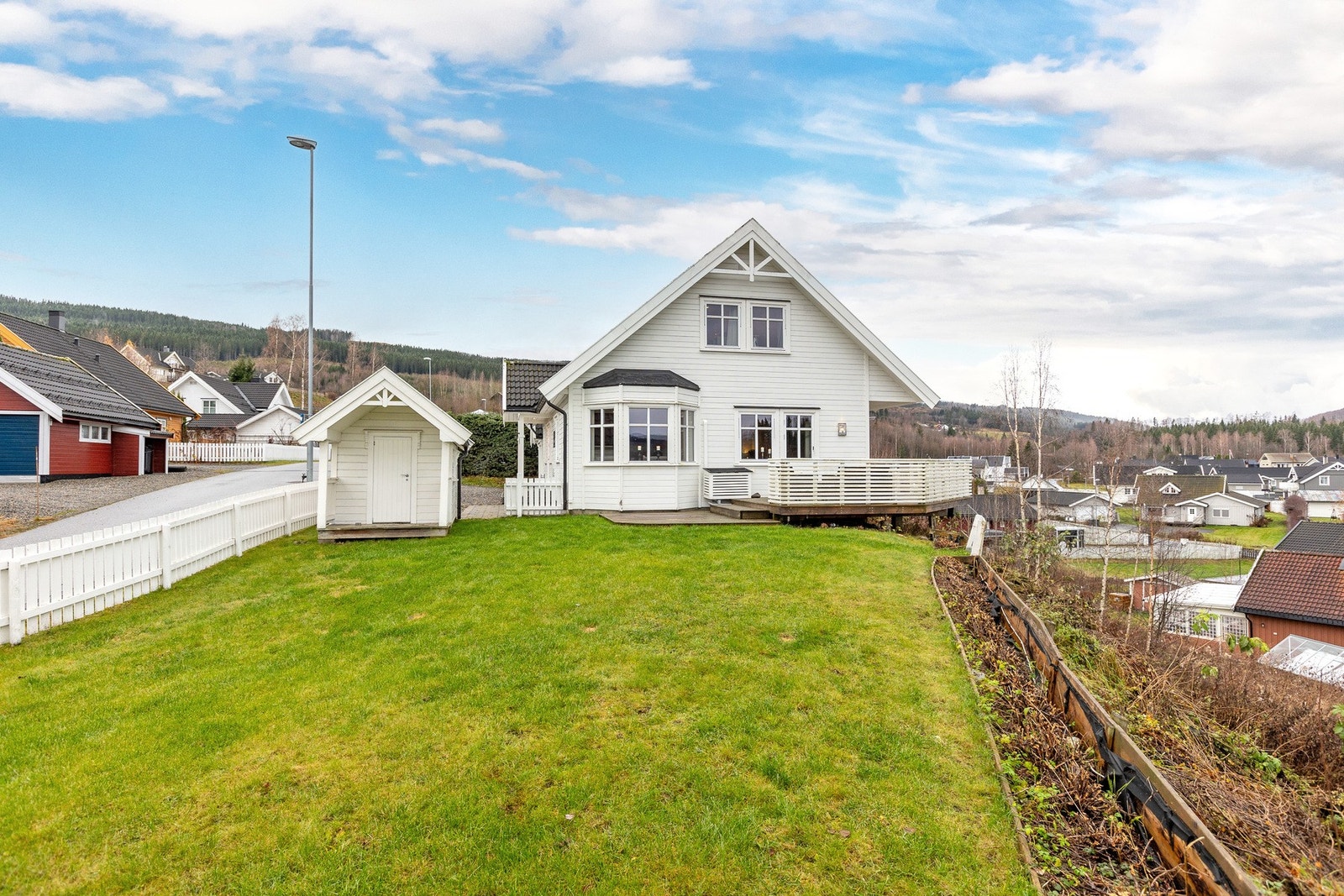 Forholdsvis flat eiet tomt som er pent opparbeidet med plenarealer og annen beplantning. Galleribilde