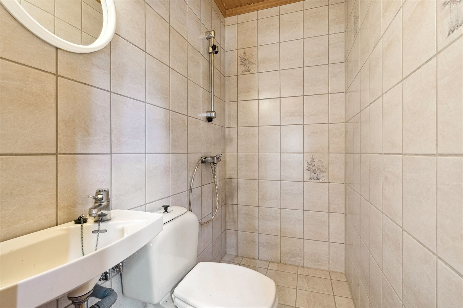 Badet har vegghengt servant, gulvstående toalett og åpen dusj i hjørne. Begge badene har flislagte vegger og gulv med varmekabler. Galleribilde