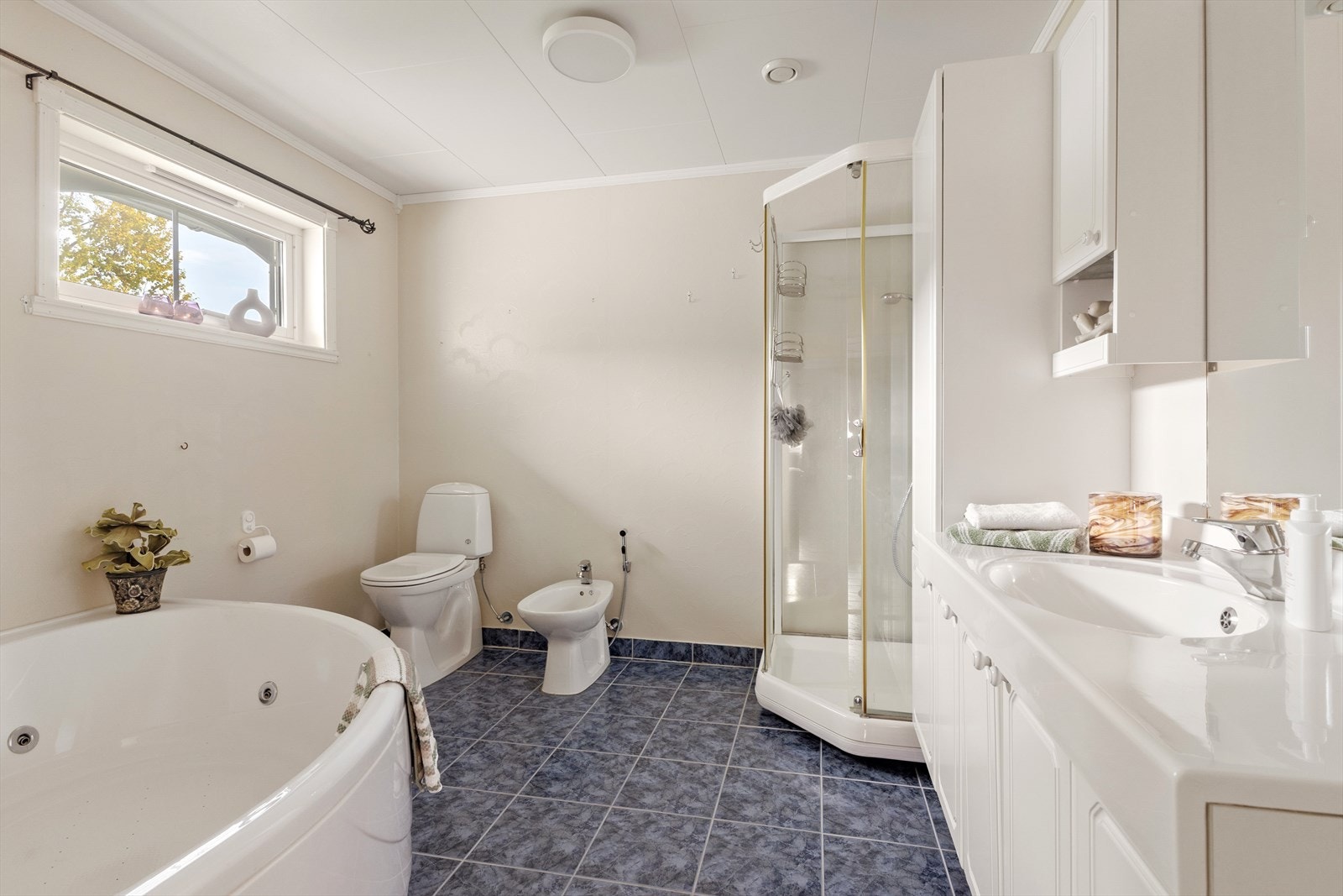 Stort, flislagt bad med plass til både badekar, dusjkabinett, toalett, bidet og en romslig baderomsinnredning. Galleribilde