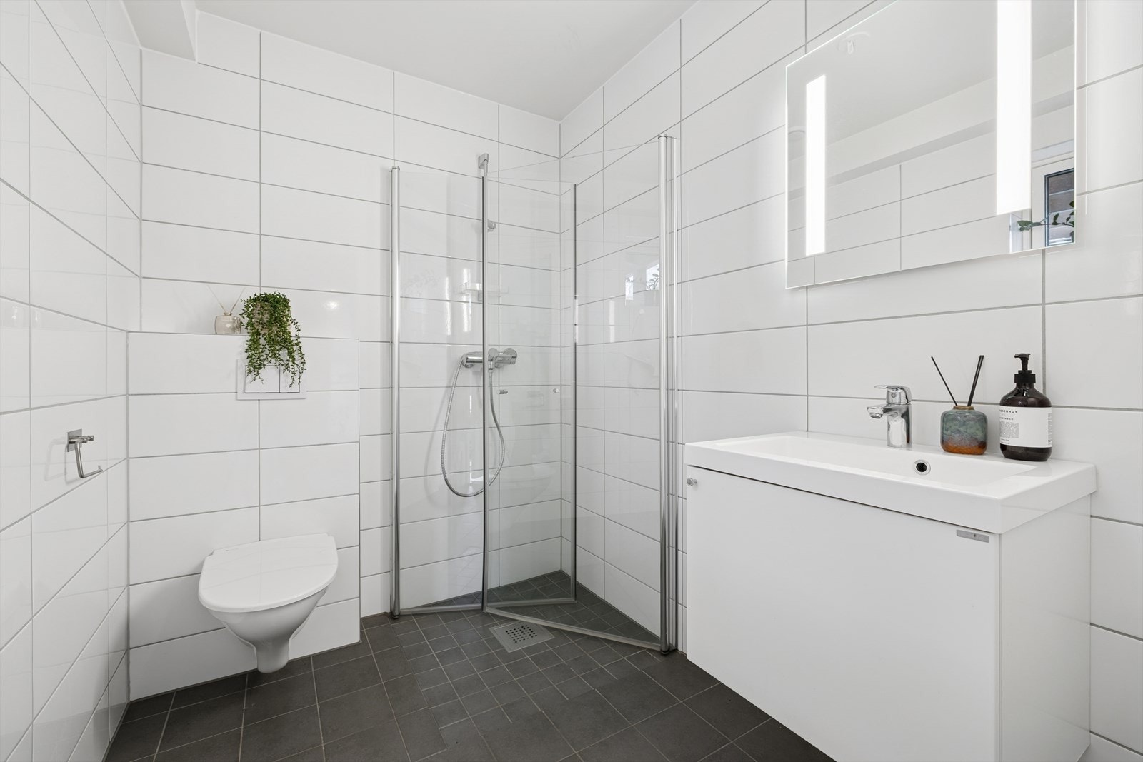 Badet i 1. etasje er fra 2020 med flislagte gulv og vegger i en stilren kombinasjon av mørke gulvfliser og lyse veggfliser. Galleribilde