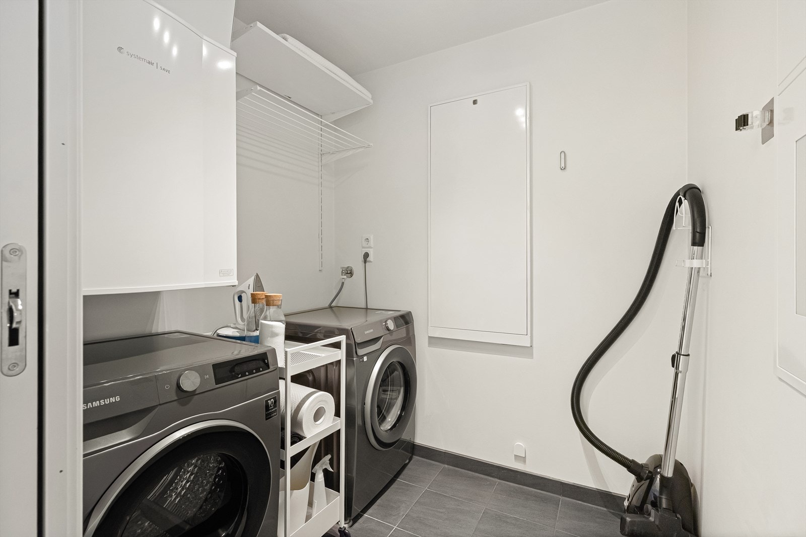 Praktisk vaskerom med moderne vaskemaskin, tørketrommel og oppbevaring. Enkelt vedlikehold med flislagt gulv og stilren design. Galleribilde