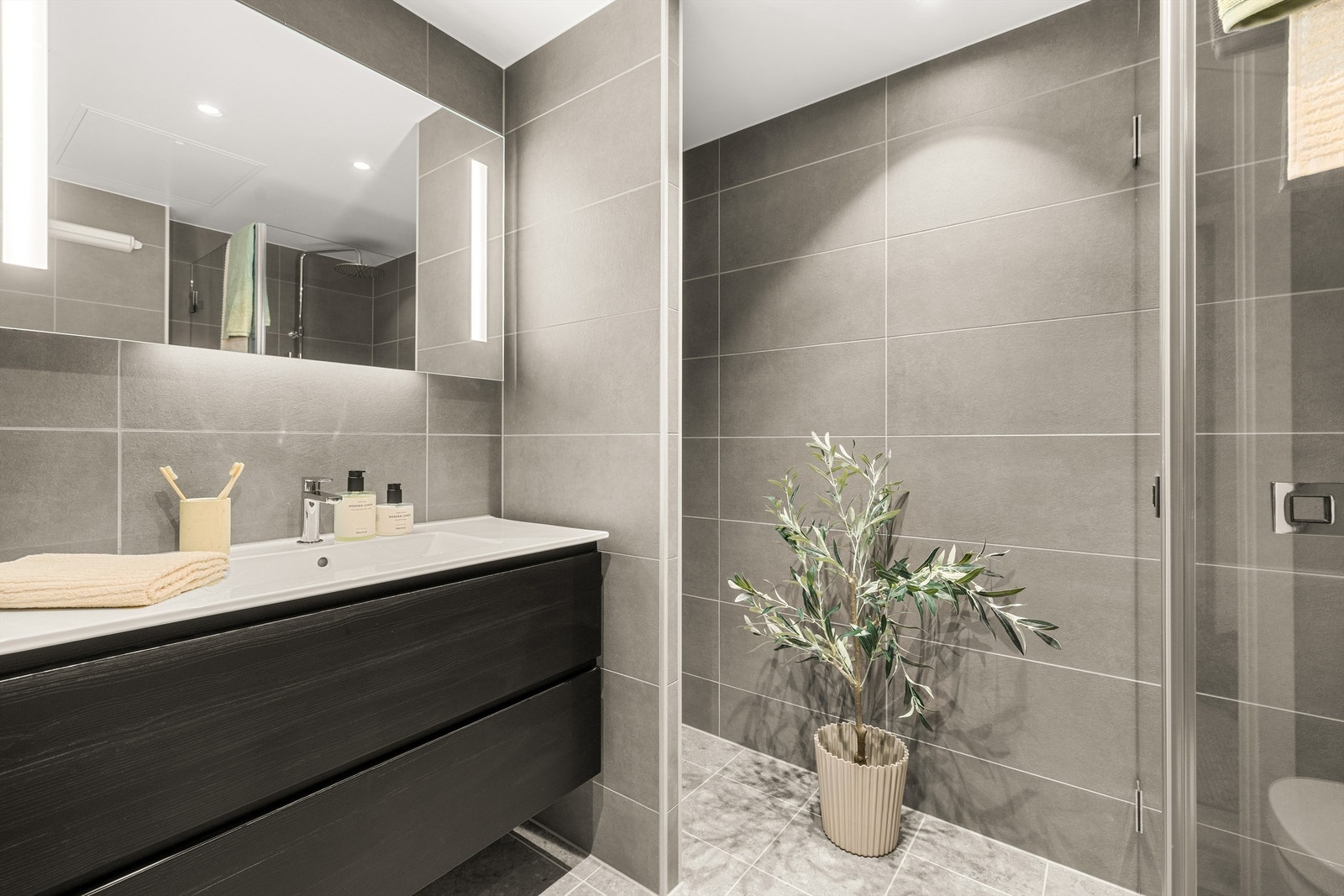 Badet leveres med delikate fliser i en greige tone med et terrazzo-uttrykk på gulv og en veggflis i samme tone Galleribilde