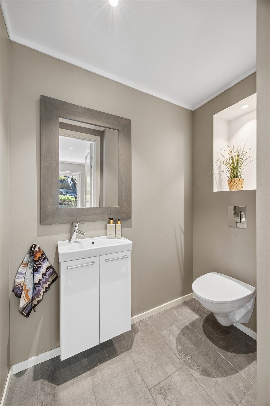 Toalettrommet har malte vegger og fliser på gulv, innredet med vegghengt toalett og baderomsinnredning med servant. Galleribilde