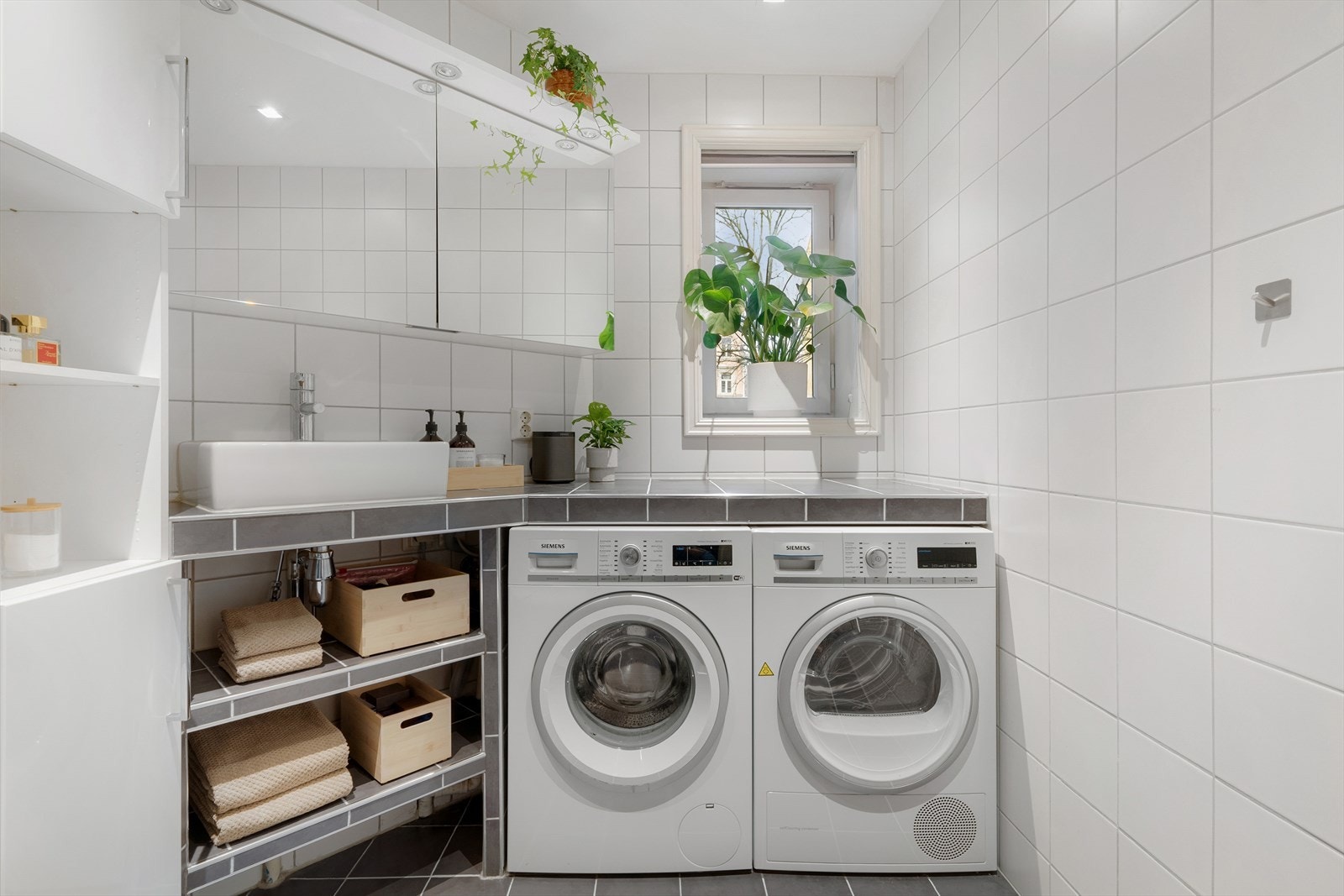 Den flislagte benken gir ekstra oppbevaringsplass og skaper samtidig en fin ramme rundt vaskemaskin og tørketrommel. Det er varme i gulv og fin downlightsbelysning i tak. Galleribilde