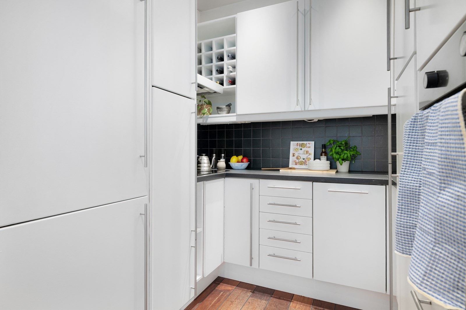 Lyse, nymalte laminerte fronter med trestruktur fra Epoq-kjøkken. Laminat benkeplate med nedfelt rustfri oppvaskkum, samt ettgreps kjøkkenbatteri. Fliser mellom over- og underskap. Galleribilde