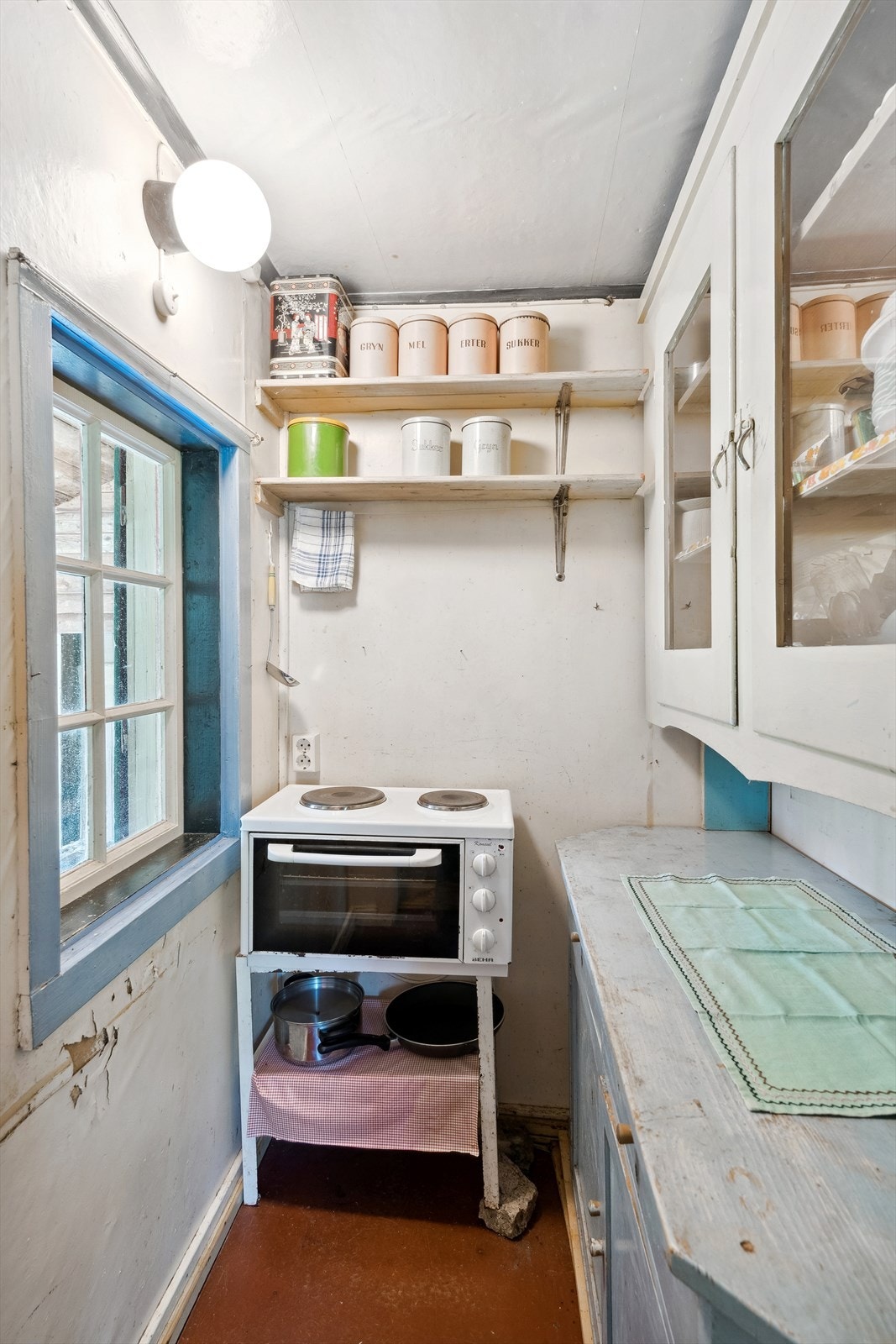 Overskapene har glassdører, og en gammel hybelkomfyr står løst i hjørnet. Galleribilde