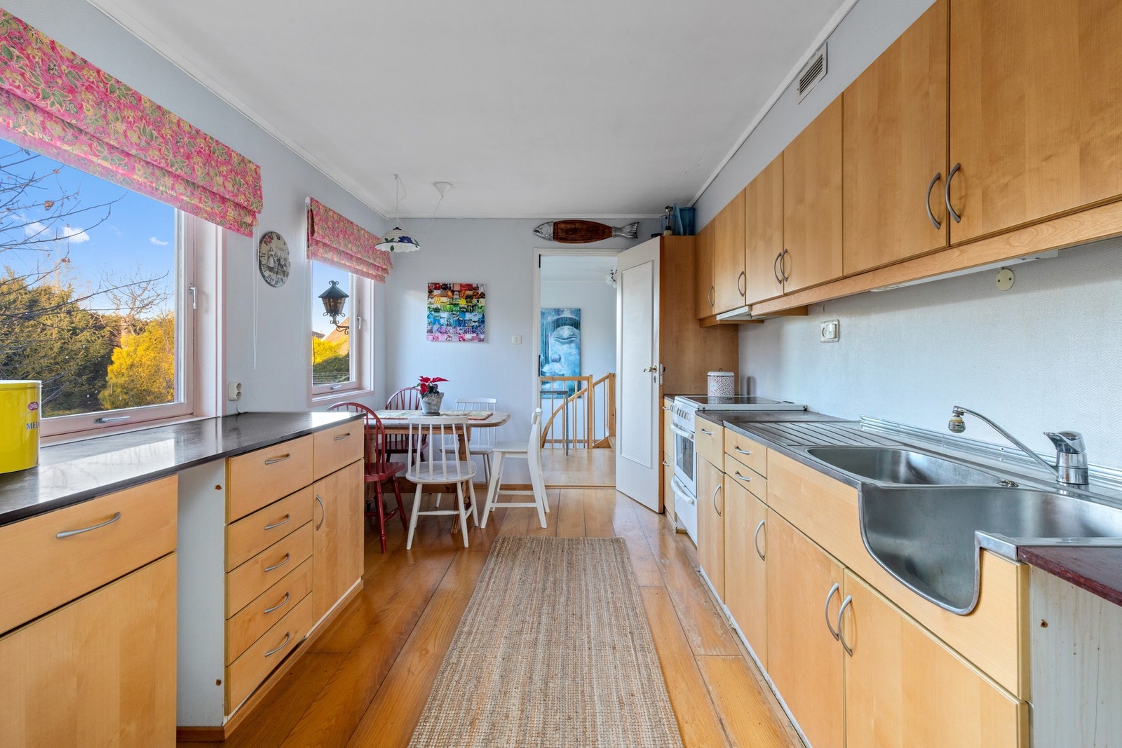 Kjøkken med spiseplass og utsyn til hagen med frukttrær. Kjøkkenet er innredet med glatte fronter og laminerte benkeplater. Galleribilde