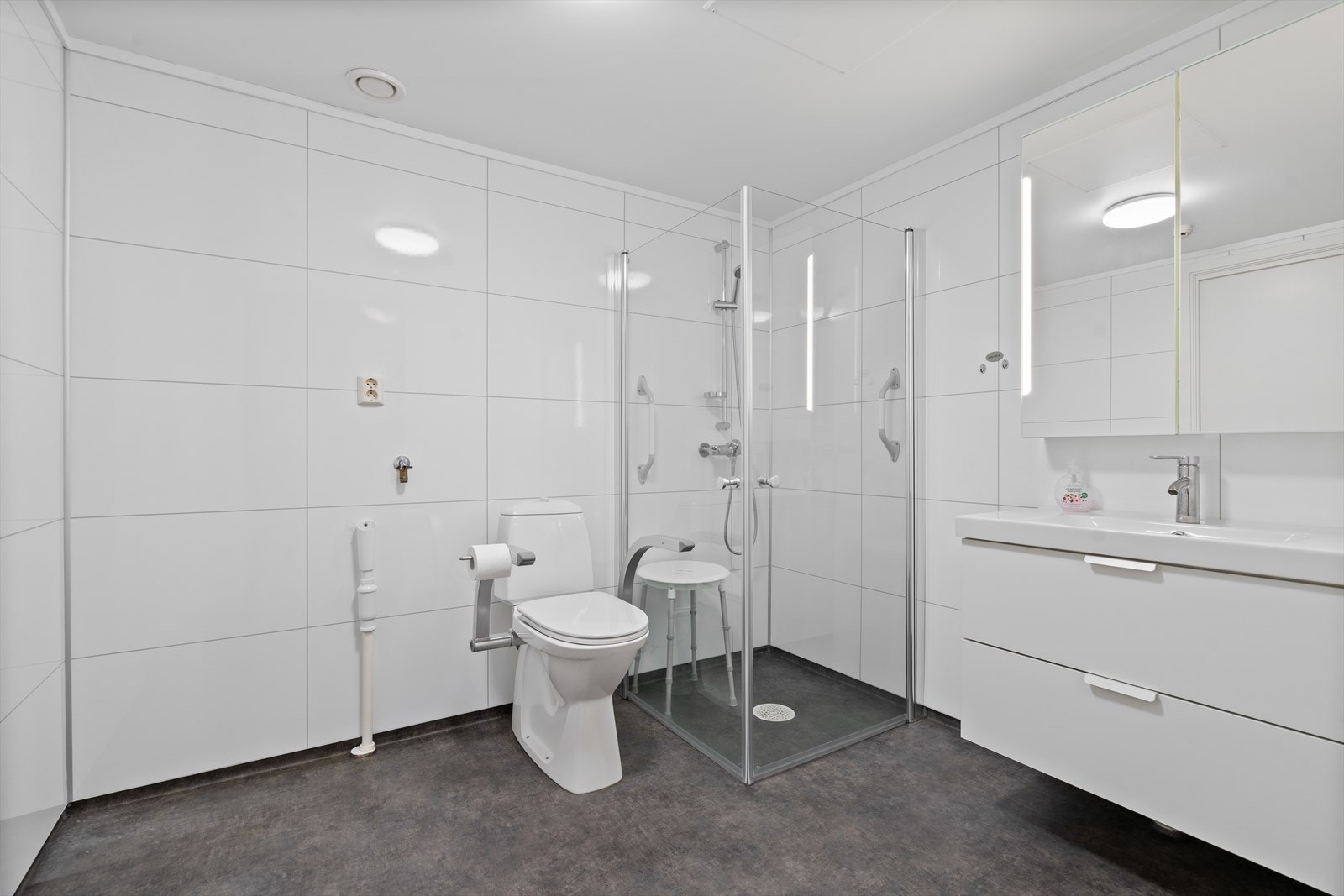 Bad/vaskerom av god størrelse, innredet med toalett på sokkel, dusjhjørne med svingbare dører og seksjon med servant. Opplegg for vaskemaskin. Det er våtromsbelegg på gulv og våtromspanel på vegg. Galleribilde