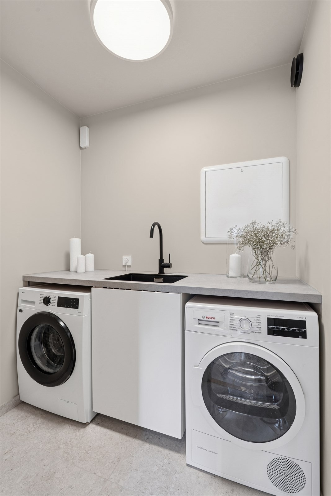 Leiligheten har eget vaskerom med flislagt gulv og malte vegger. Her er plass for både vaskemaskin og tørketrommel, og det er praktisk arbeidsbenk med vask. Galleribilde