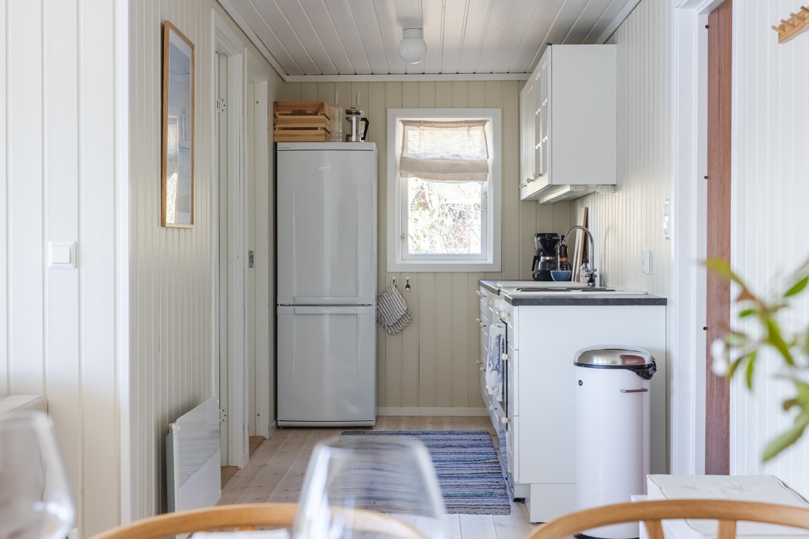 Kjøkkeninnredningen fra 2010 ligger tilbaketrukket, plassert langs én vegg innerst i rommet. Innredningen har hvite, profilerte fronter, noen vitrineskap med belysning og benkeplate i mørk laminat med nedfelt vaskekum. Galleribilde