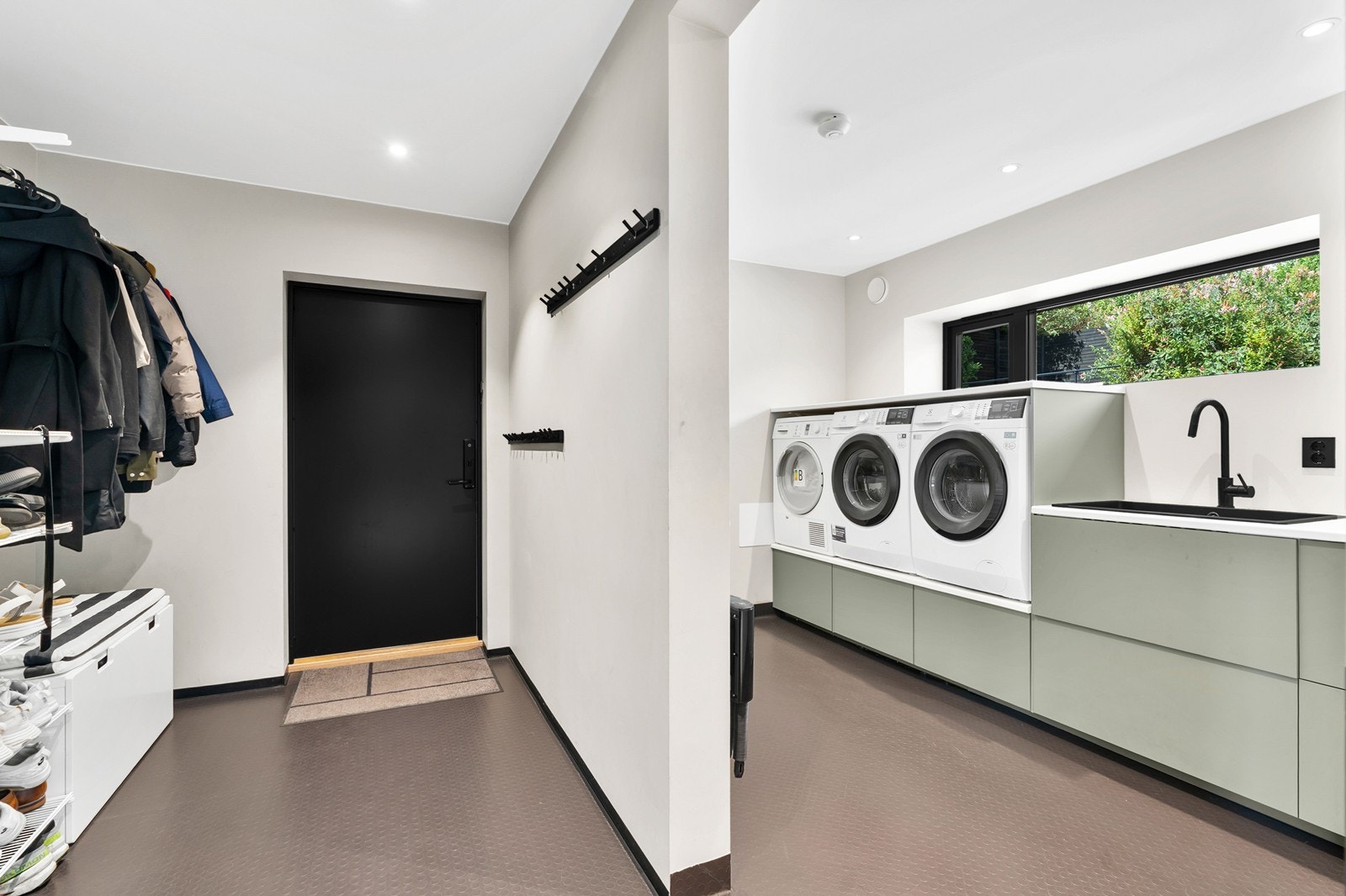 Stort og praktisk vaskerom med gulvbelegg med varmekabler, malte plater på vegg og i tak. Det er spotter i tak. Rom er innredet med 2 vaskemaskiner, tørketrommel og utslagsvask. Galleribilde