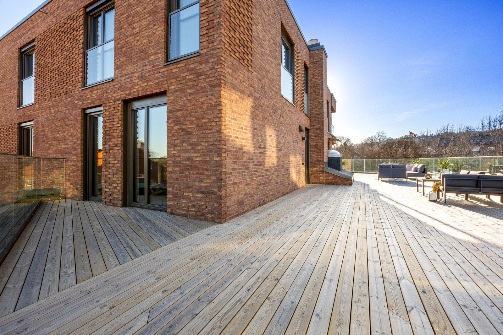 Hele terrassen har dekke av terrassebord, rekkverk i glass og diskret vegglamper i sort design. Galleribilde