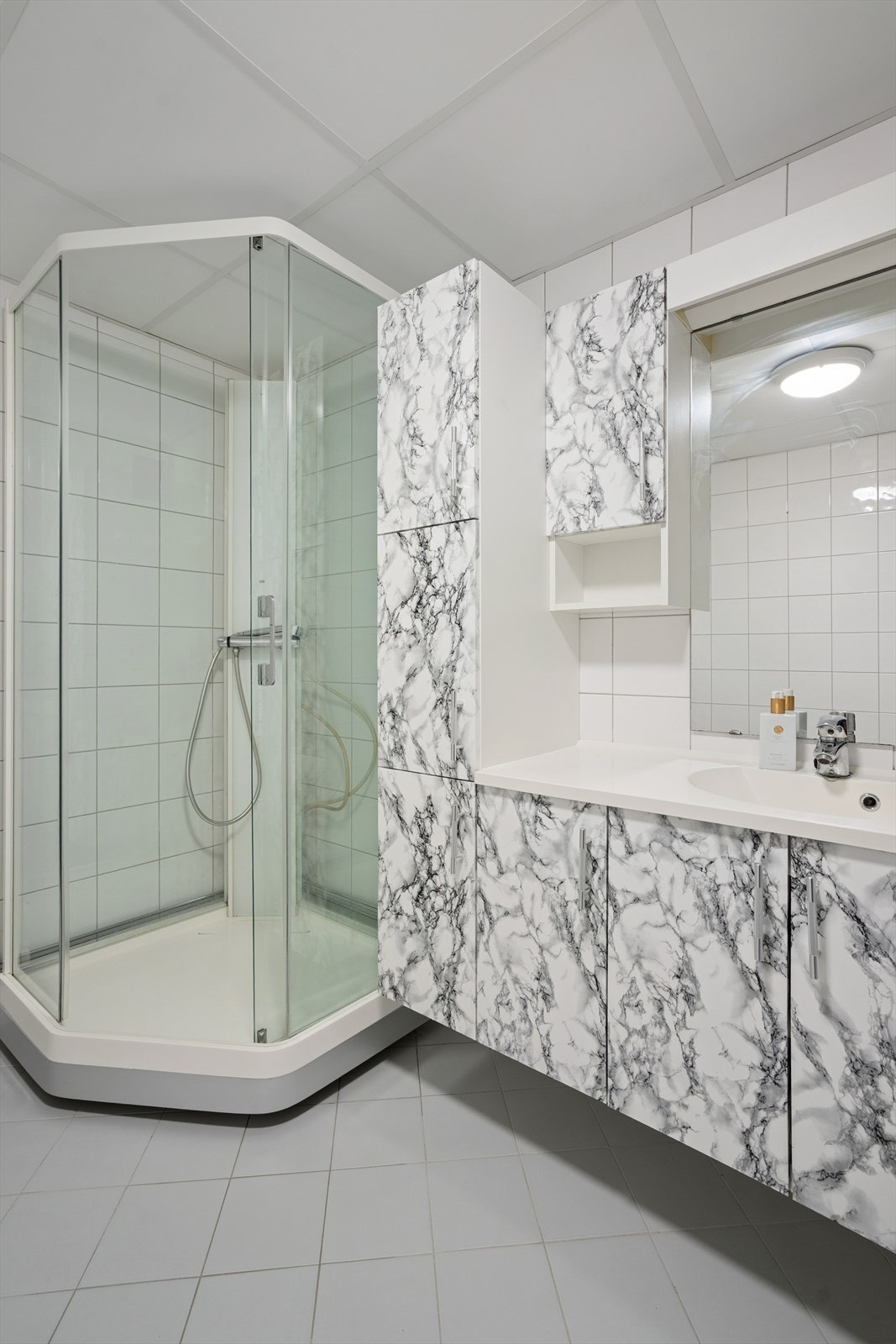 Baderomromsinnredningen består av benkeskap med heldekkende servant, speil, toalett og et dusjkabinett. Galleribilde