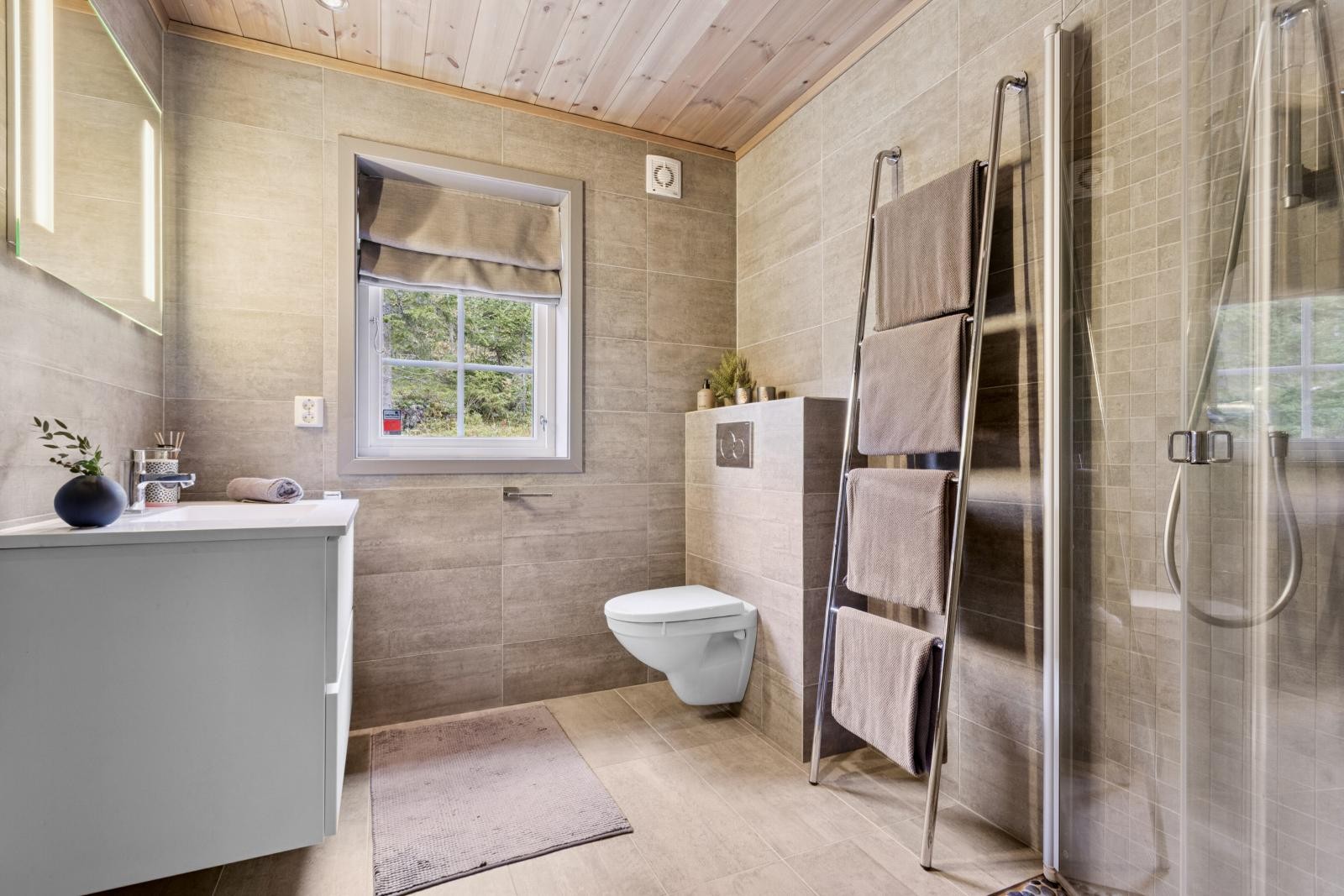 Stort hovedbaderom med vegghengt wc, servant med underskap og veggmontert speil med sidebelysning. Stort dusjhjørne med innfellbare glassdører og videre inngang til badsturommet Galleribilde