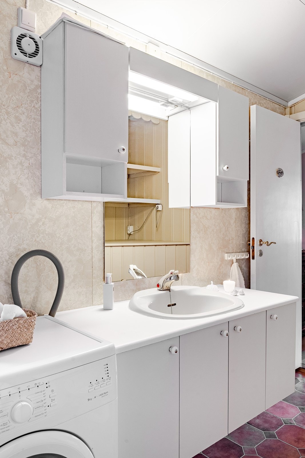 Lys baderomsinnredning med nedfelt servant, speil med belysning og vegghengte skap over. Plass og opplegg for vaskemaskin ved siden av. Galleribilde