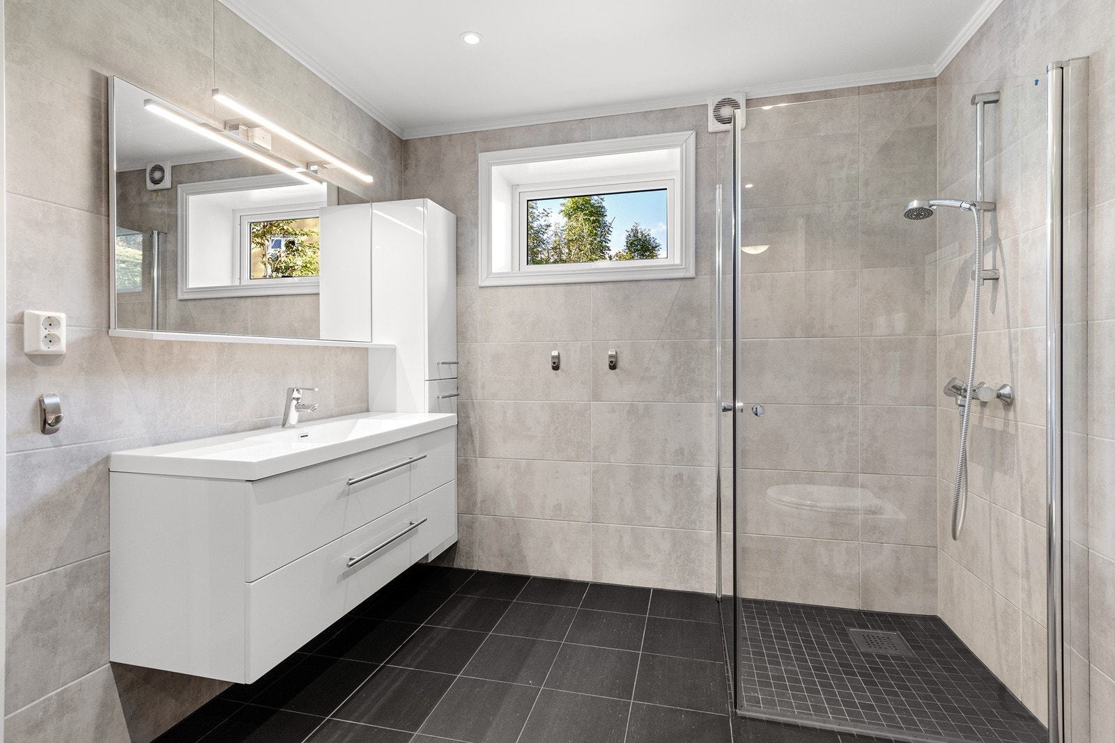 Bad inneholder innredning med servanttopp, dusjhjørne med glassdører, og vegg-wc. Opplegg til vaskemaskin. Fordelerskap montert på baderom. Galleribilde