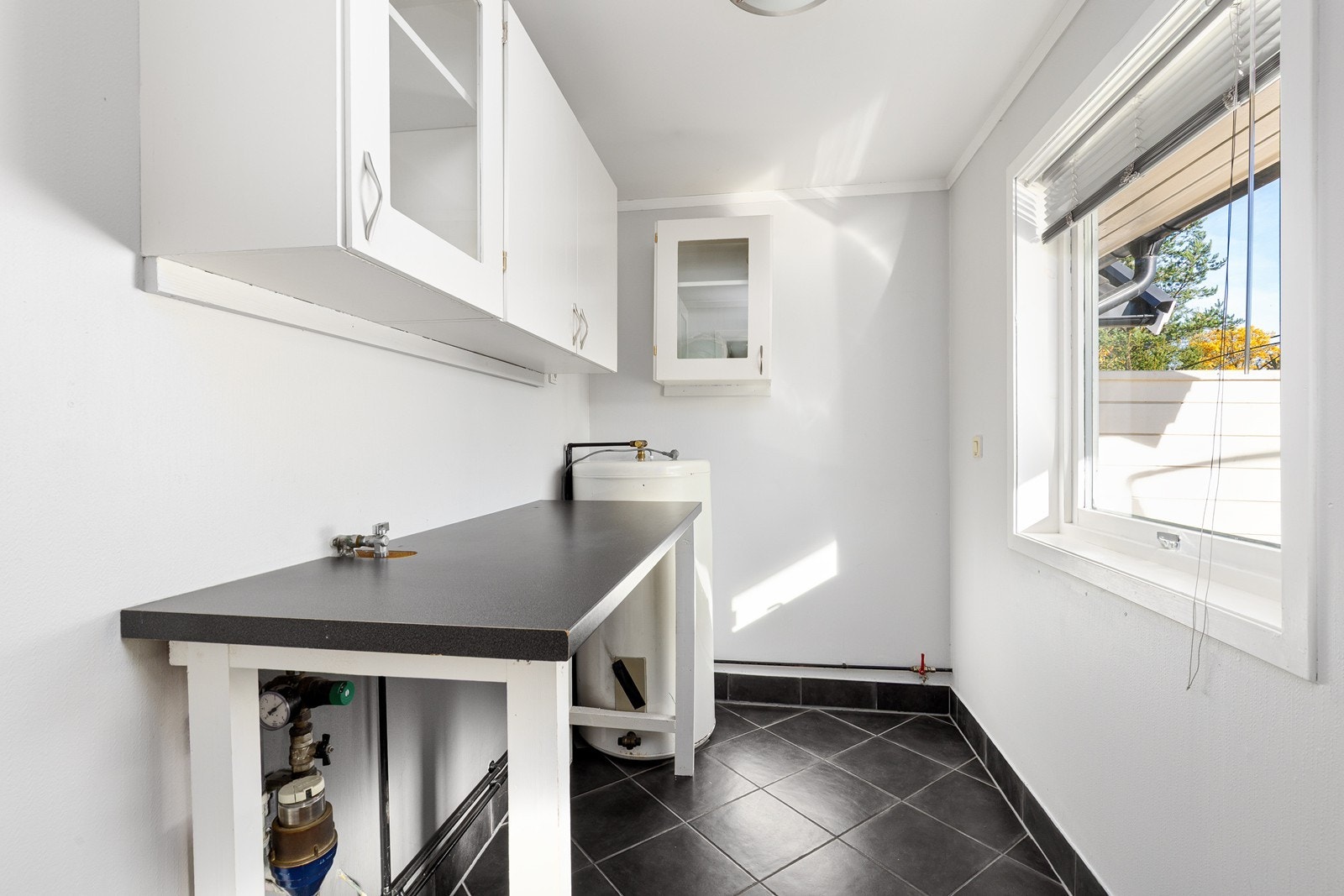 Praktisk innredet vaskerom med fliser på gulv og tapetserte vegger. Rommet har innredning med overskap og noe benkeplass. Opplegg for vaskemaskin. Galleribilde