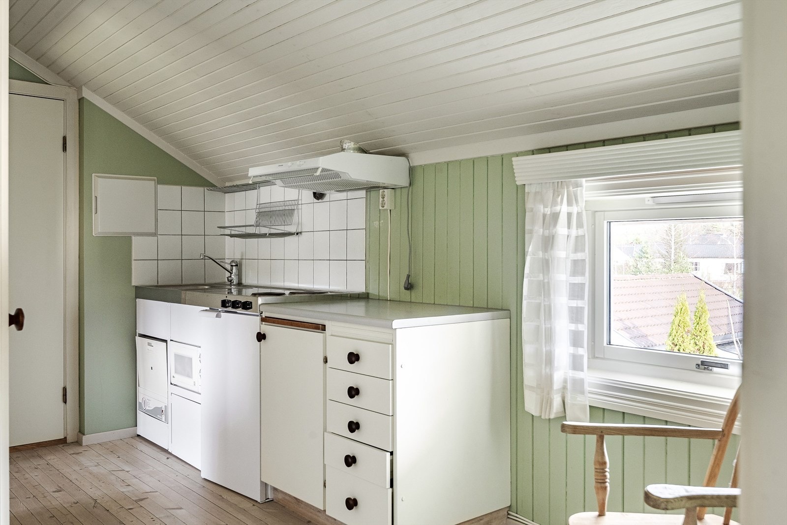 Enkel eldre kjøkkeninnredning i 2. etasje med lyse fronter og fliser i benkeryggen. Kjøkkenet er utstyrt med integrert oppvaskmaskin, mikrobølgeovn og kjøleskap. Galleribilde