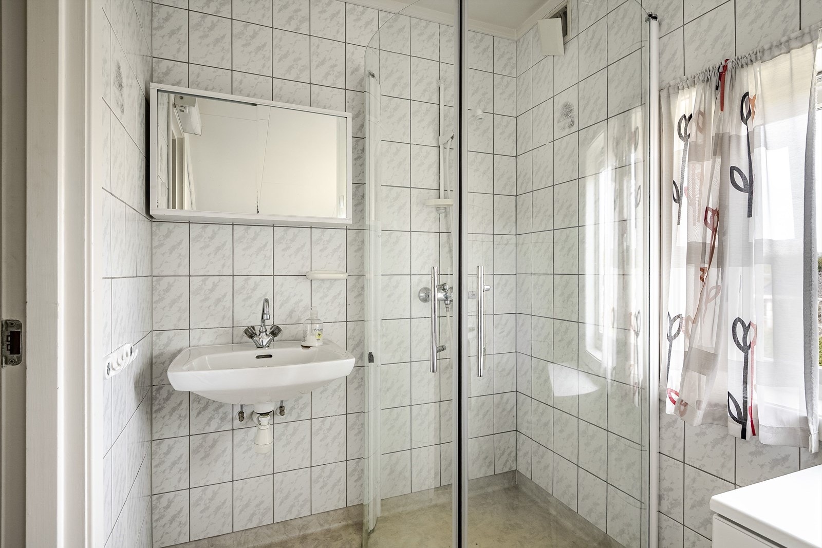 Eldre baderom i 2. etasje med våtromsbelegg på gulv og fliser på veggene. Baderommet er utstyrt med vegghengt servant, speilskap, dusjhjørne med glassdører og opplegg for vaskemaskin. Galleribilde