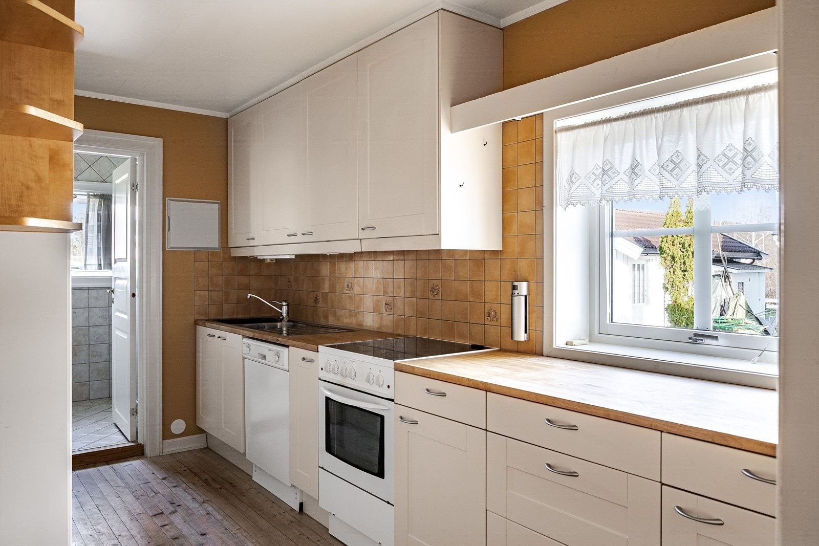 Kjøkkeninnredning med lyse profilerte fronter og heltre benkeplate med nedfelt oppvaskkum. Praktisk med fliser i benkeryggen og belysning under overskap. Galleribilde