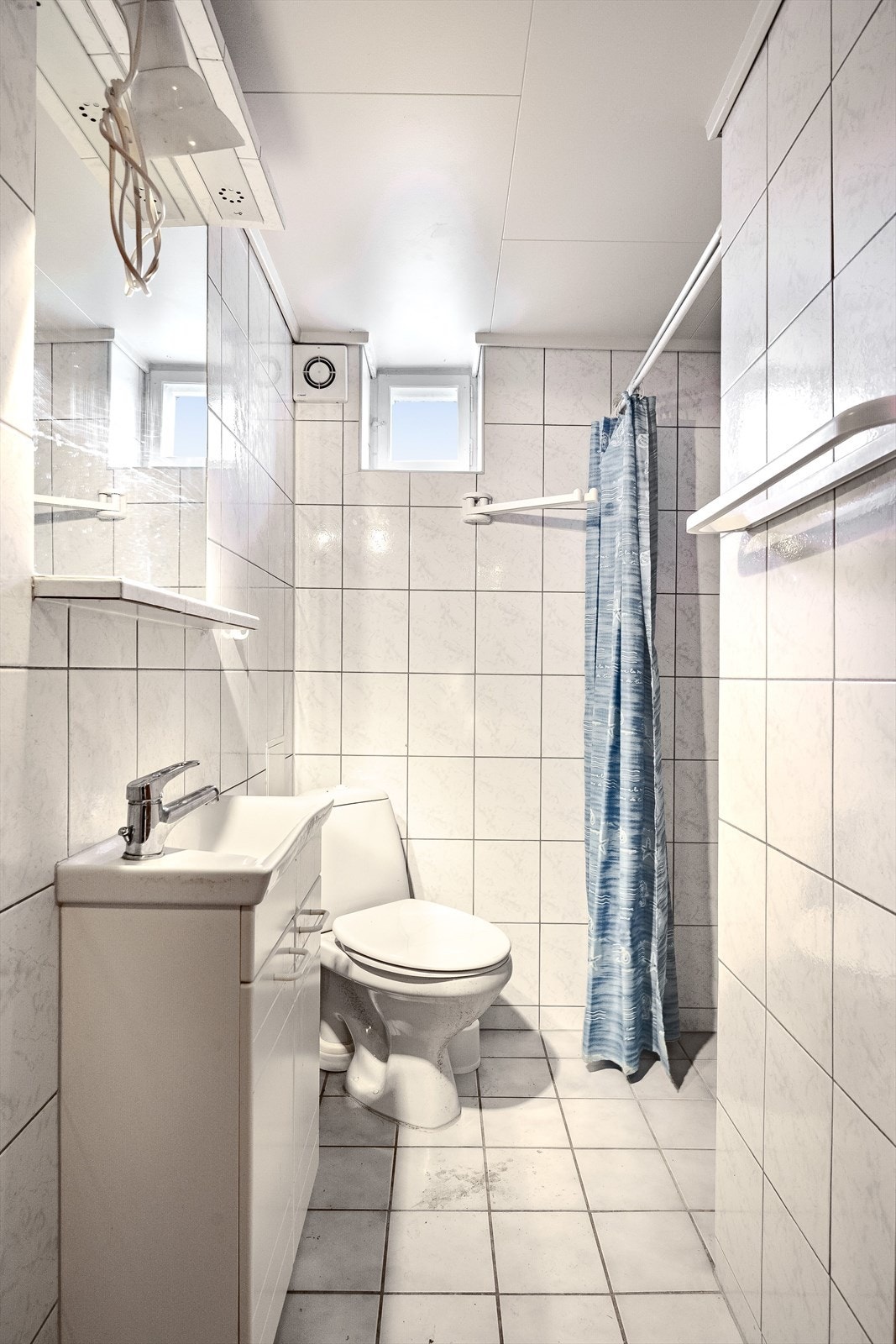 Baderom i kjeller med overflater, installasjoner og komponenter fra ca. 2005. Baderommet har fliser på gulv og vegger, gulvvarme og elektrisk styrt vifte. Galleribilde