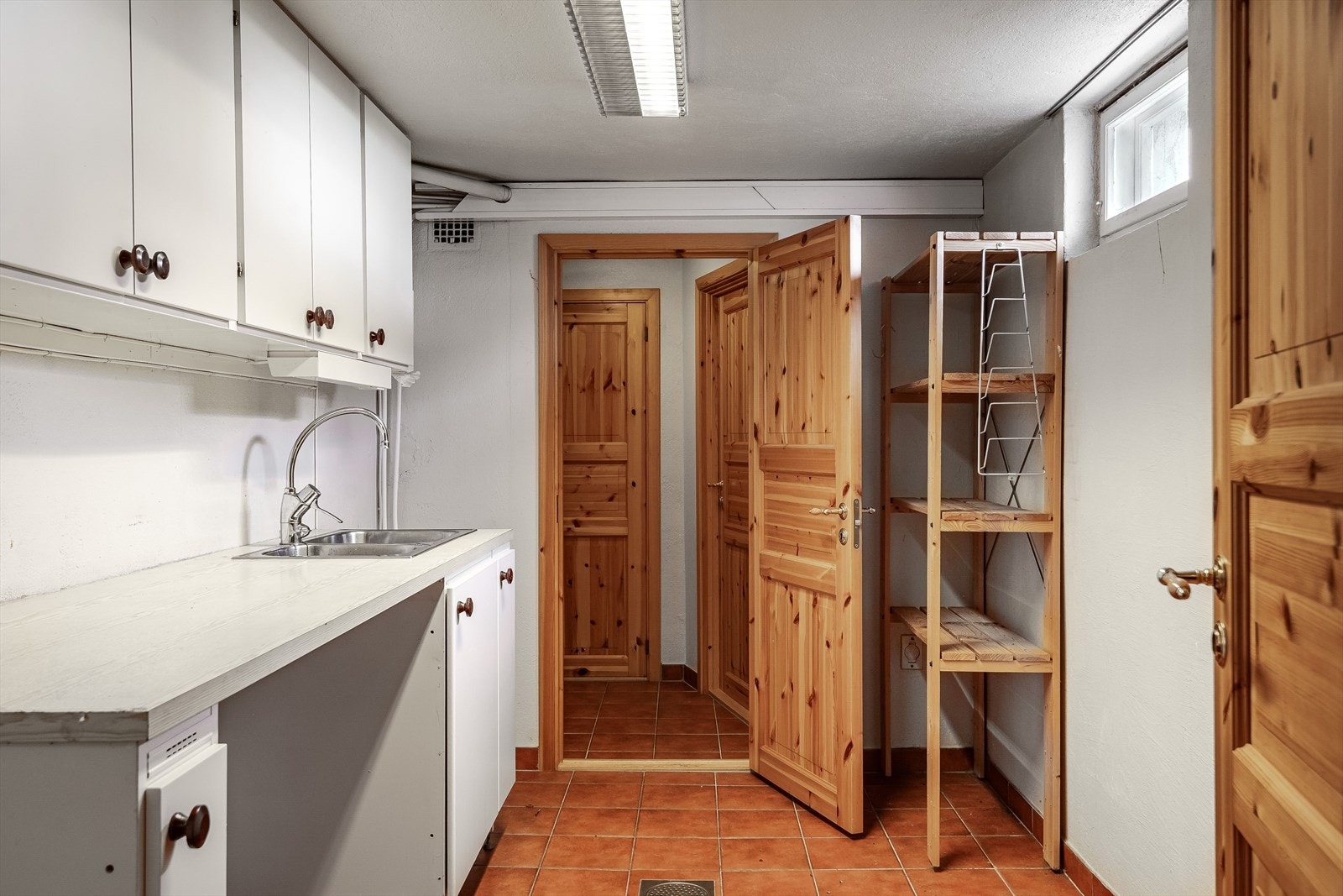 Eldre innredning i kjeller med lyse fronter og laminert benkeplate med nedfelt oppvaskkum. Galleribilde