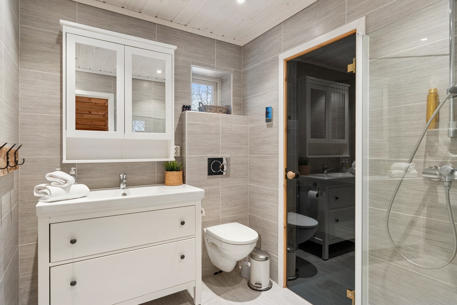 Flislagte vegger og beiset panel i himling gir en solid og estetisk løsning på badet. Dusjhjørne med innfellbare dusjvegger og elektrisk styrt vifte sikrer effektiv ventilasjon. Galleribilde