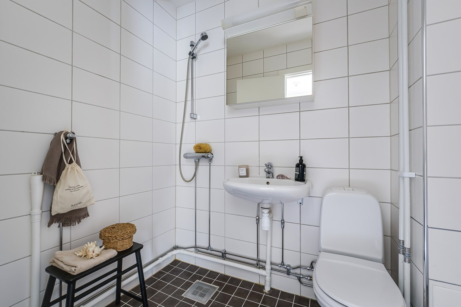 Flislagt baderom med frittstående toalett, vegghengt servant, speilskap med lys. Det er opplegg for vaskemaskin. Galleribilde