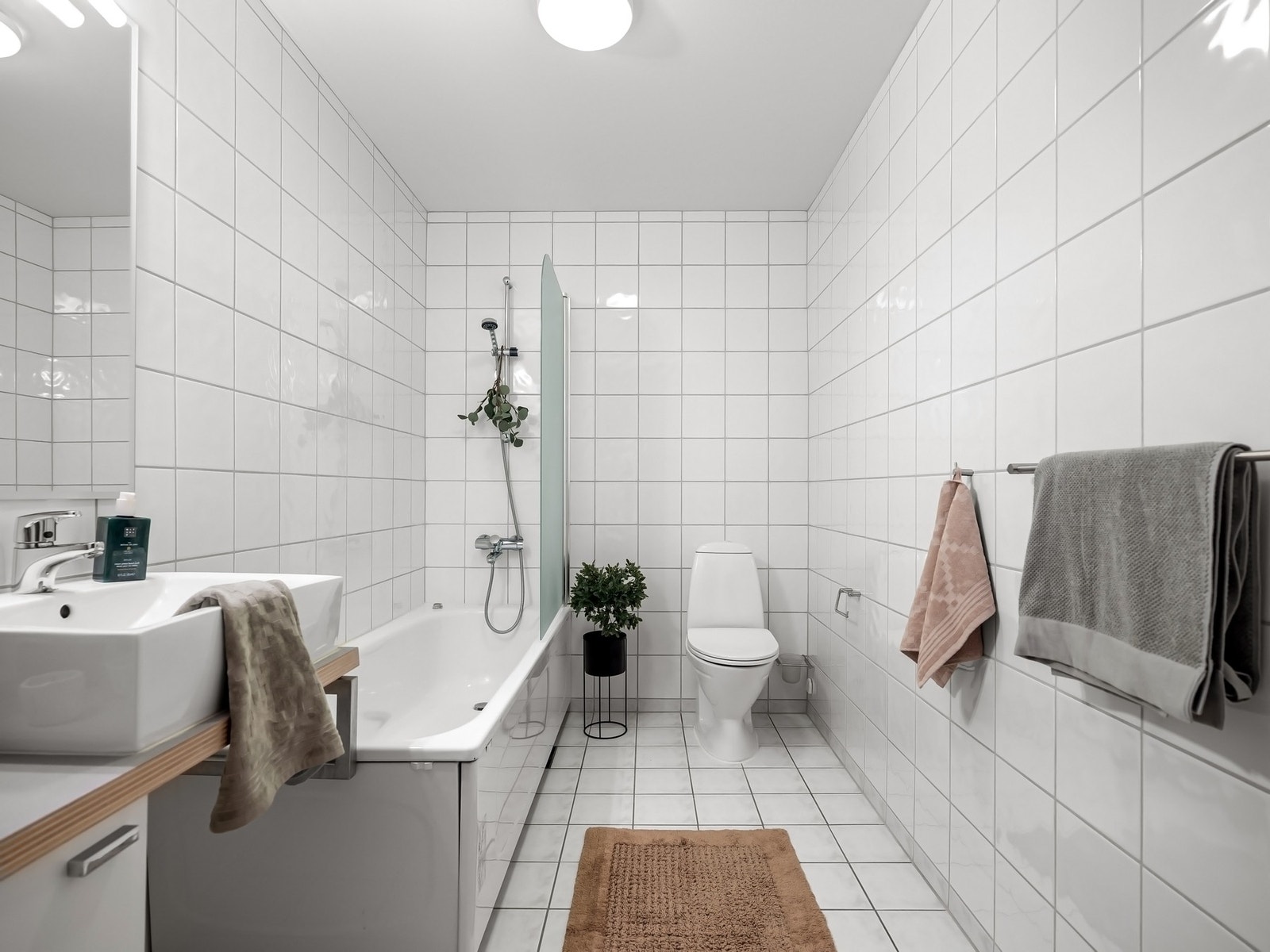 Lekkert og funksjonelt bad fra byggeåret med flislagte vegger i 20x20-format som gir et rent og klassisk uttrykk. Badet er innredet med servant med oppbevaringsbenk under, speil på vegg og et komfortabelt badekar med frontpanel og svingbar glassvegg Galleribilde
