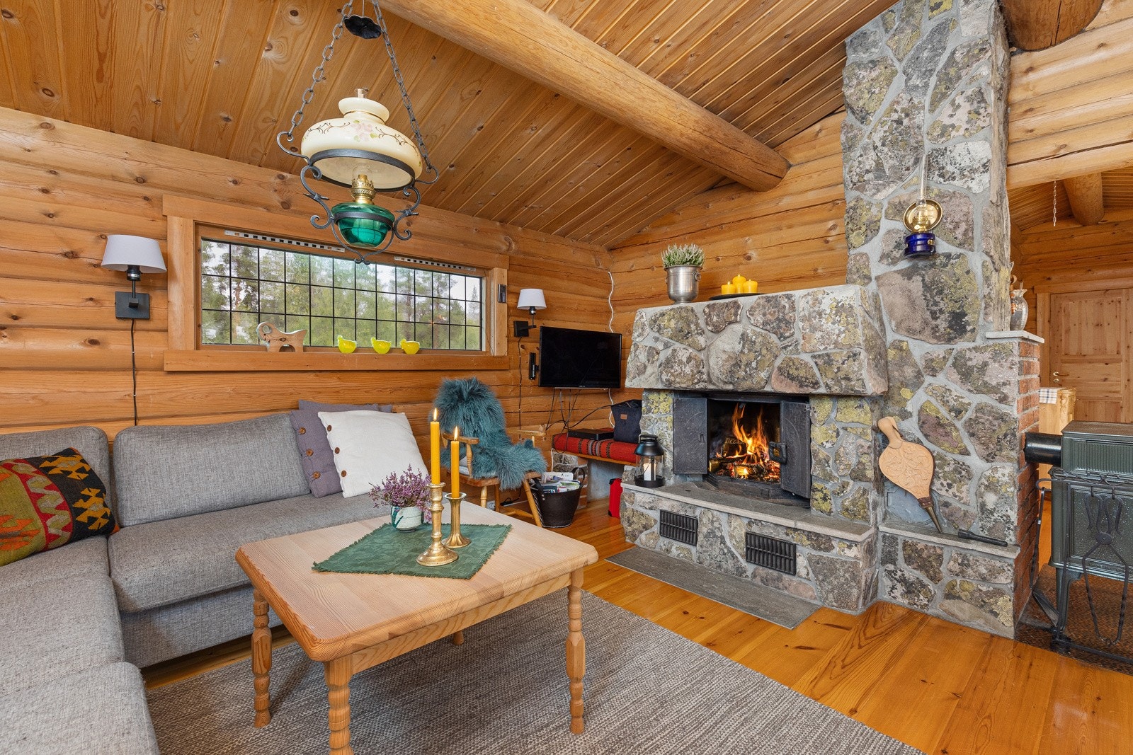 Den koselige hytta har en hyggelig atmosfære med sine tømmervegger og mønet tak. I tillegg er et blyglassvindu og en stor peisinnsats kledd i naturstein som blir en fin interiørdetalj. Galleribilde