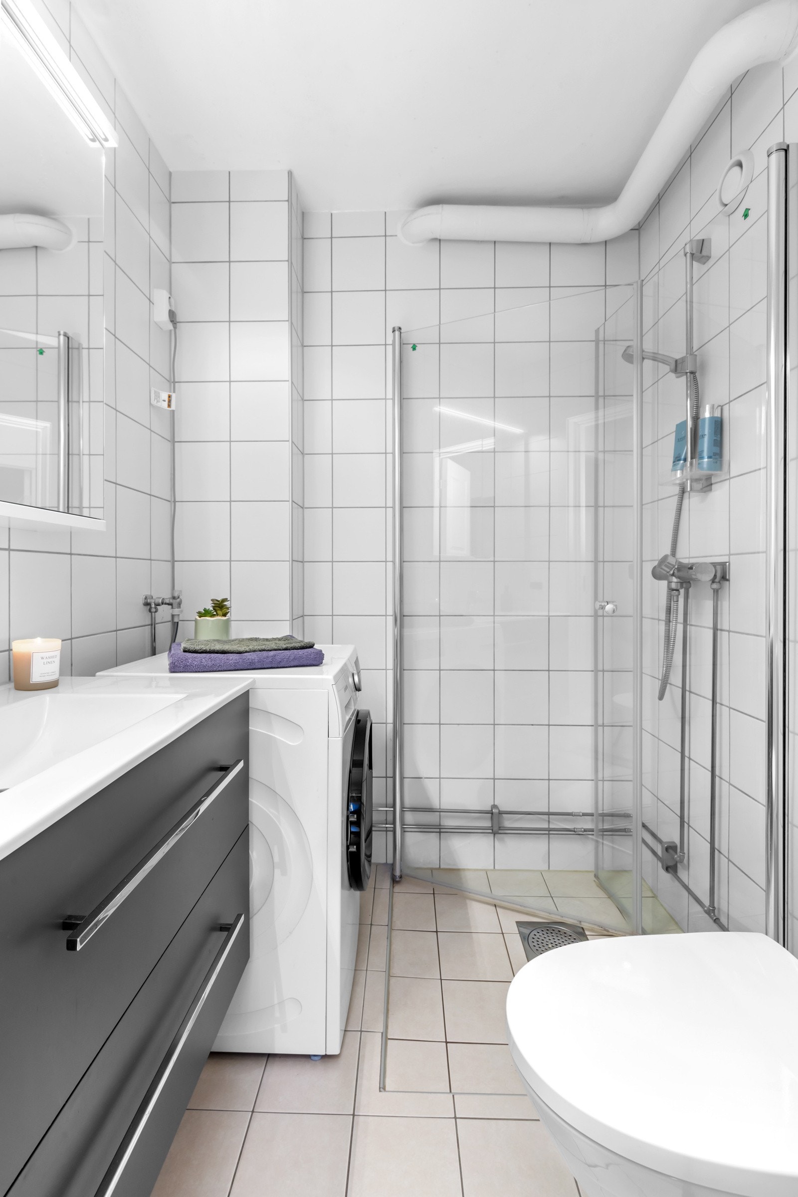 Flislagt bad med dusjnisje, vaskemaskin, vask og toalett Galleribilde