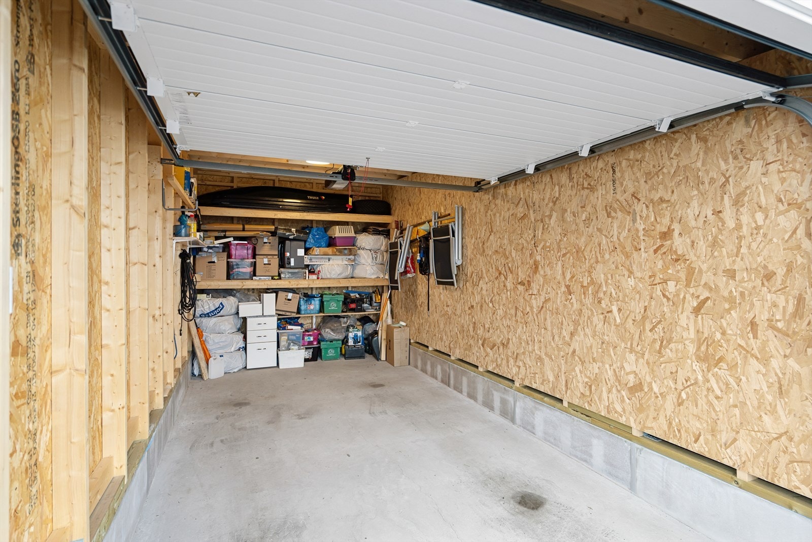 Garasjeport med automatisk portåpner. Praktiske hyller for oppbevaring er montert innerst i garasjen. Galleribilde