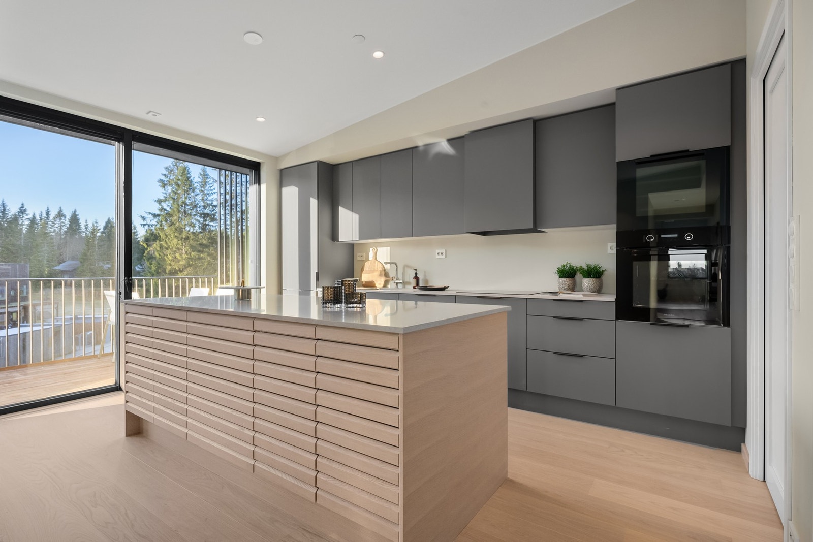 Innredningen har slette fronter i fargen Mørk Sand, brunelokserte Line-grep og en elegant kjøkkenøy i hvitpigmentert eik som gir et moderne og harmonisk uttrykk. Galleribilde