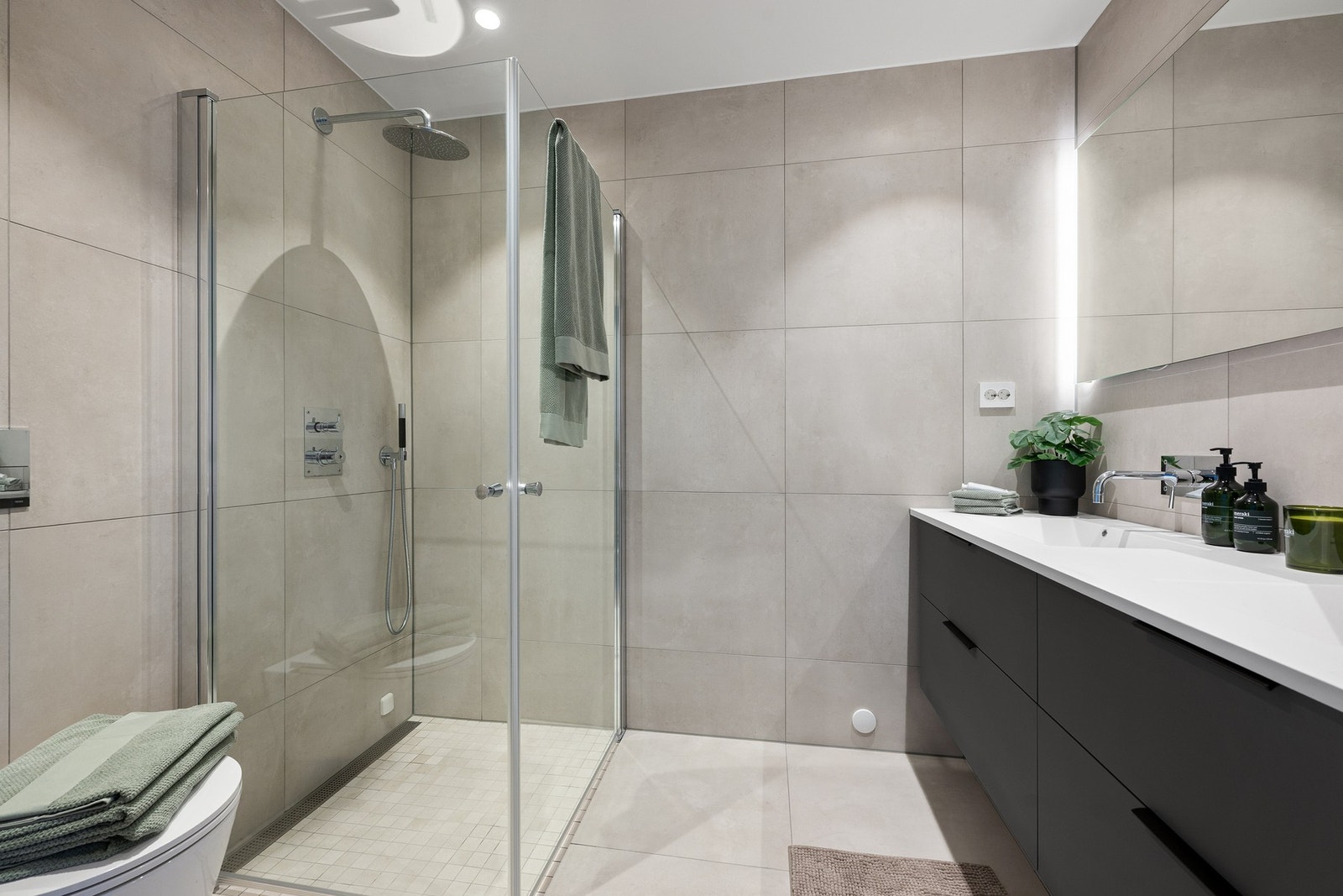 Smakfullt og delikat bad tilknyttet hovedsoverommet, innredet med dobbel servant, dusj i herdet glass og vegghengt toalett. Galleribilde