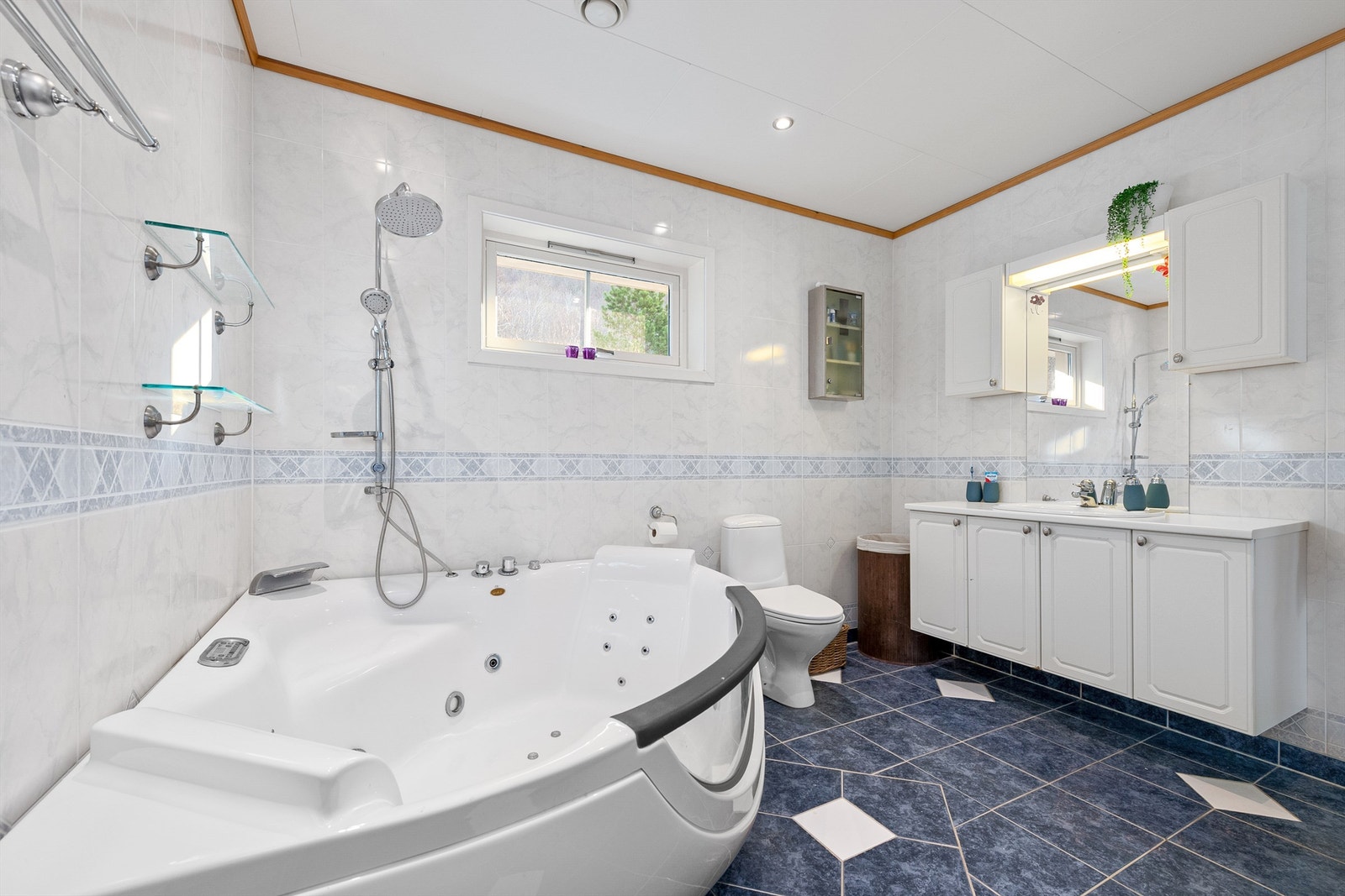 Badet har stor baderomsinnredning med profilerte fronter og ovenpåliggende servant. Speil og skal over servant. Gulvstående toalett. Galleribilde