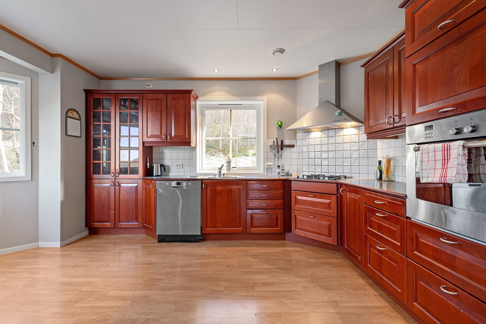 Kjøkkeninnredning fra HTH med profilert fronter i kirsebærfiner. Det er ventilatorhette over integrert koketopp med gassbluss, integrert stekeovn, opplegg for vaskemaskin. Galleribilde