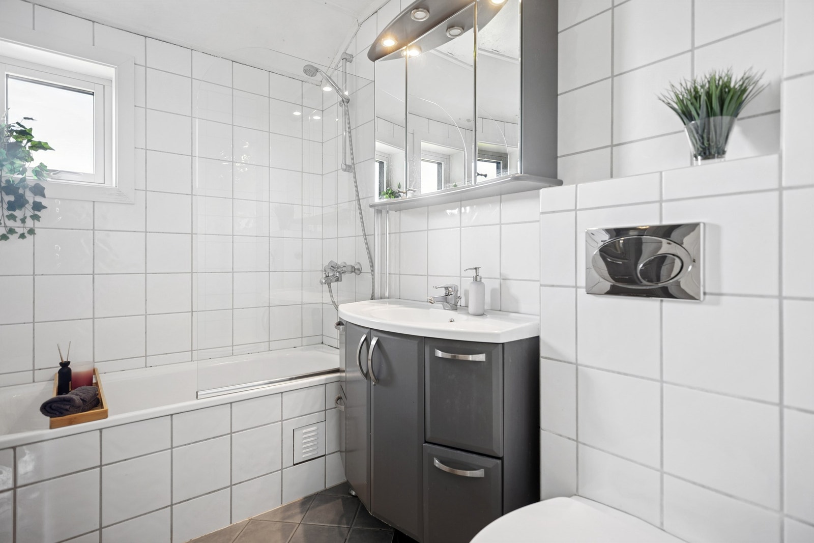 Pent flislagt bad med innebygd badekar, servantinnredning med skuffer og skap, speilskap og vegghengt toalett. Galleribilde