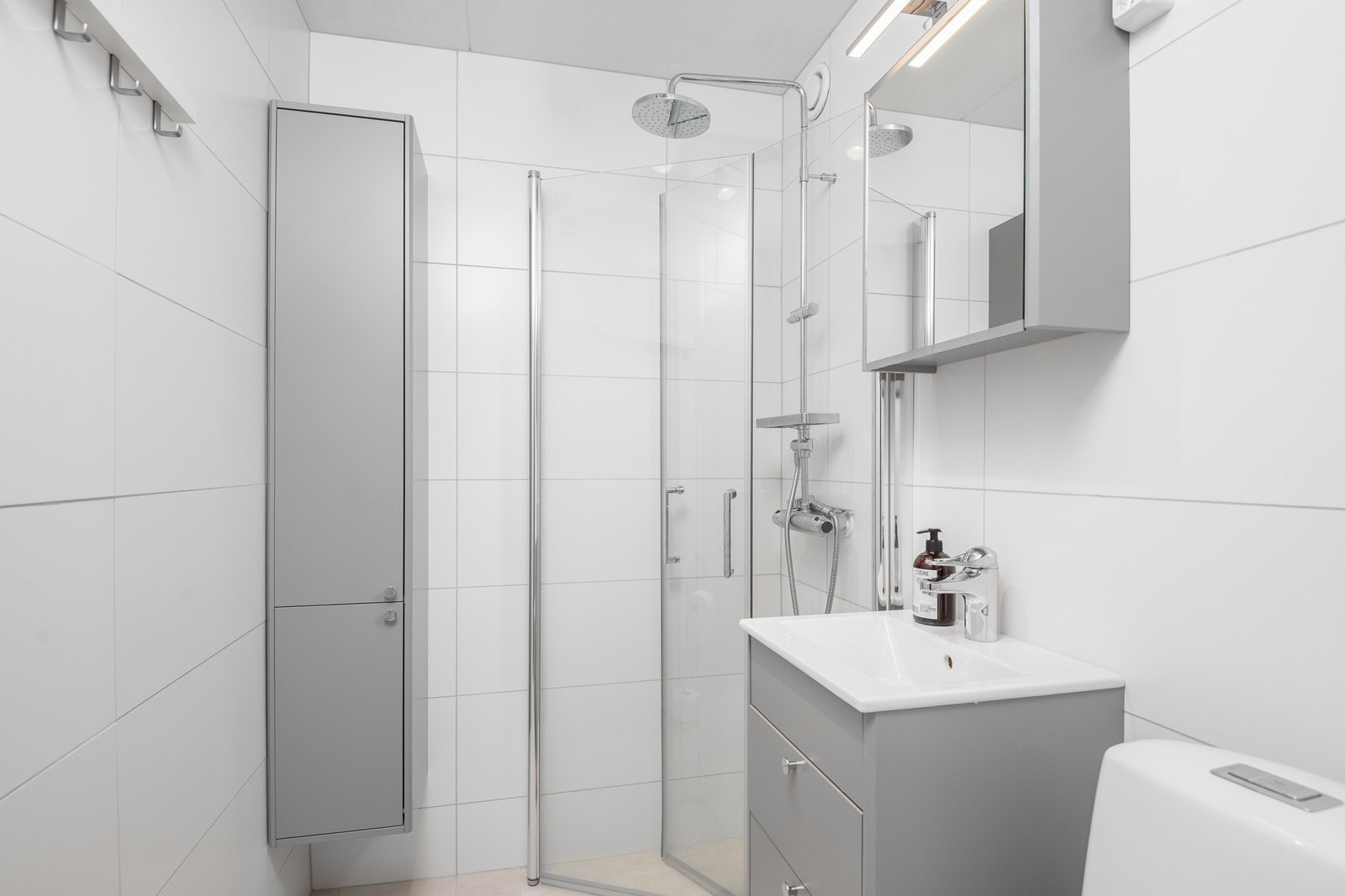 Helfliset bad med dusjhjørne, toalett, baderomsinnredning med speilskap og tilhørende høyskap. Badet er på lik linje med resten av leiligheten holdt i en lys og moderne stil. Badet har gulvvarme. Galleribilde