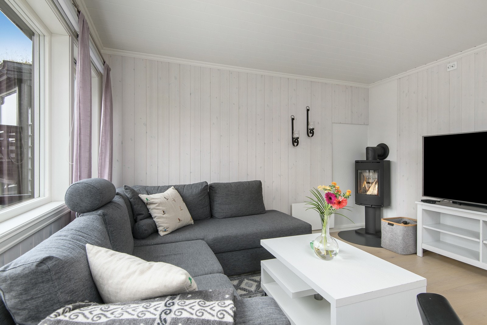 Stuen oppleves moderne med lys panel på vegg og enstavsparkett på gulv. Galleribilde