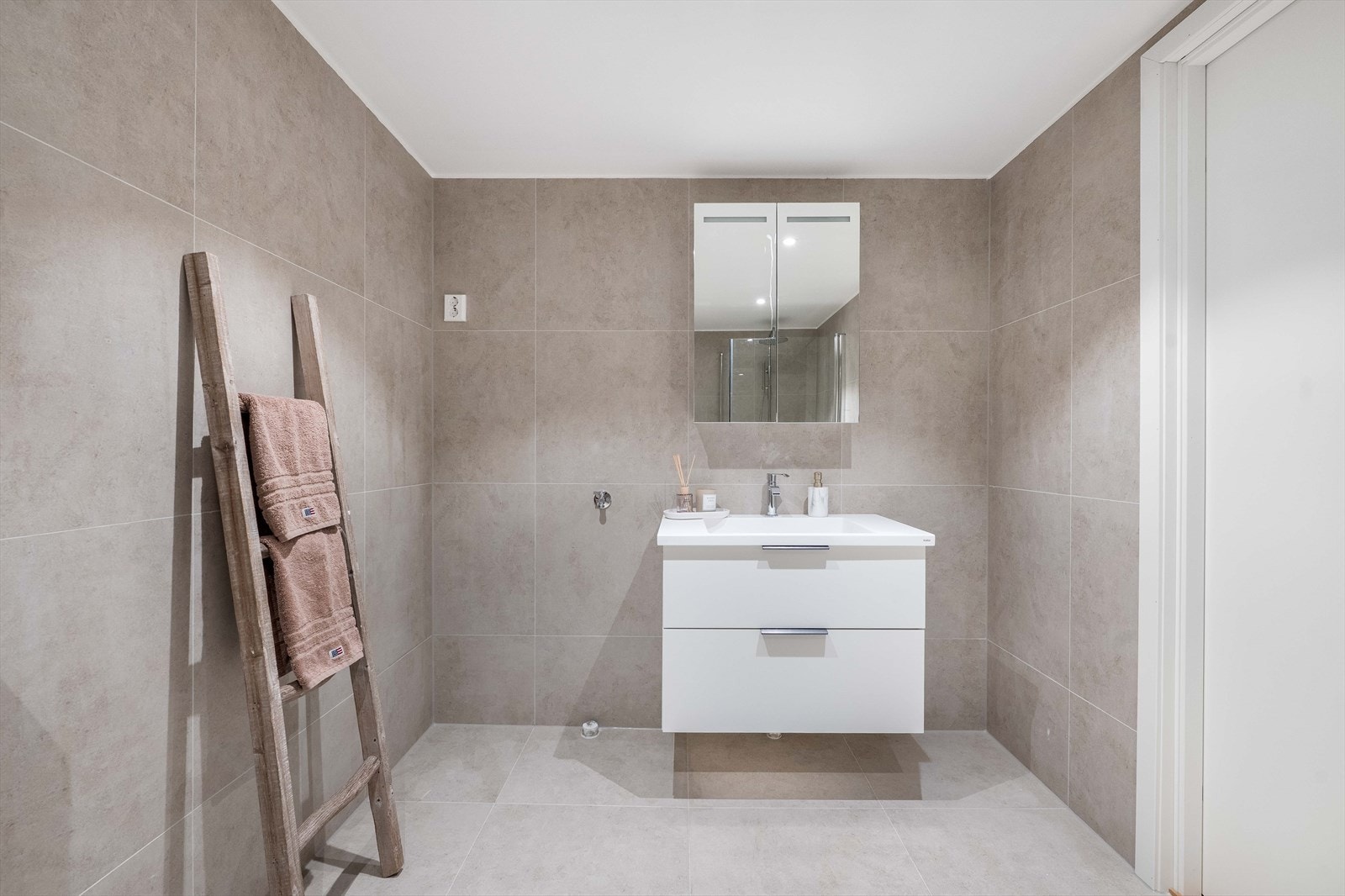 Badet har servant med slette fronter, veggmontert toalett, dusjvegger/hjørne og opplegg for vaskemaskin Galleribilde