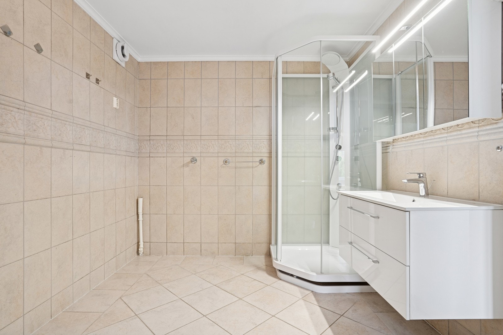 Romslig og moderne baderom med lyse fliser, dusjkabinett og innredning med god oppbevaringsplass. Galleribilde