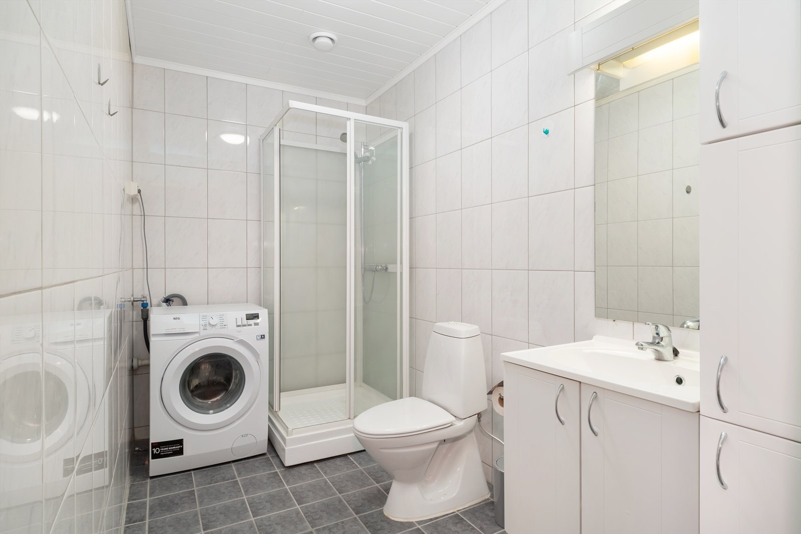 Badet er heilfilsa og utstyrt med dusjkabinett, toalett, nedfelt servant med oppbevaring og vaskemaskin. Galleribilde