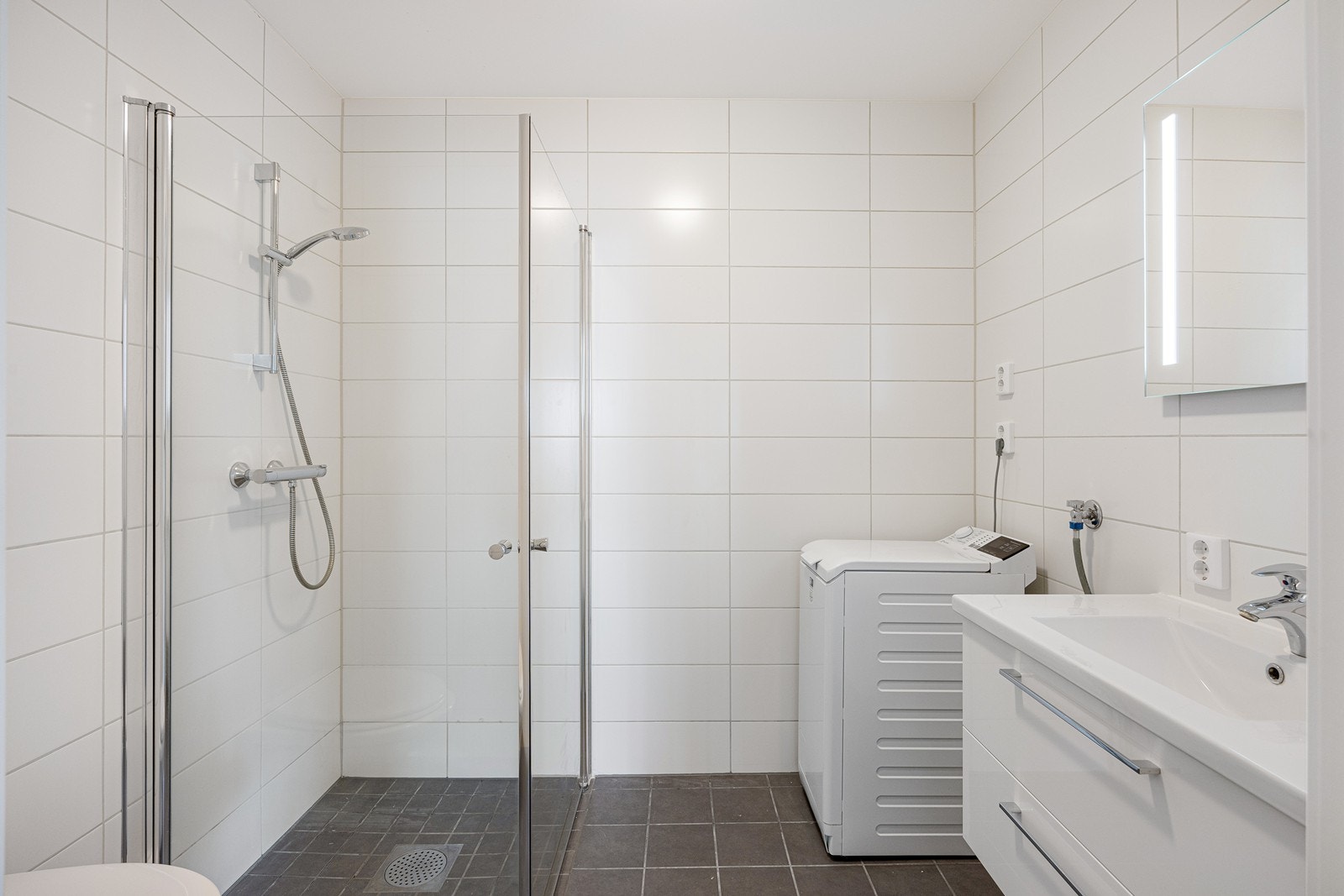 Innredningen har hvite, glatte fronter, heldekkende servant på en skuffeseksjon og et stort speil med integrert belysning. Videre er det vegghengt toalett, opplegg for vaskemaskin og et dusjhjørne med innfellbare glassdører. Galleribilde