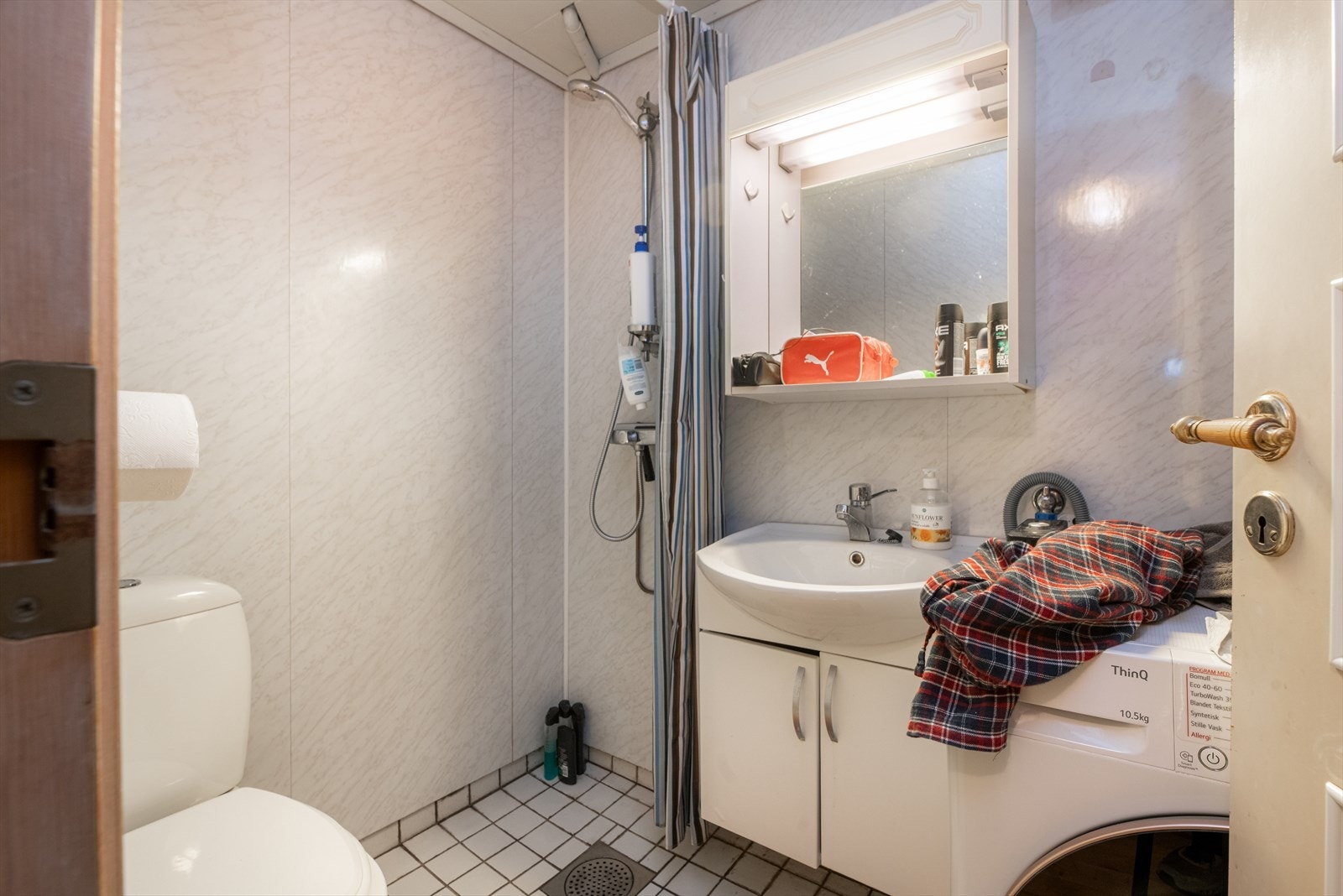 Bad med toalett, dusjhjørne, servantmøbel og opplegg for vaskemaskin. Galleribilde