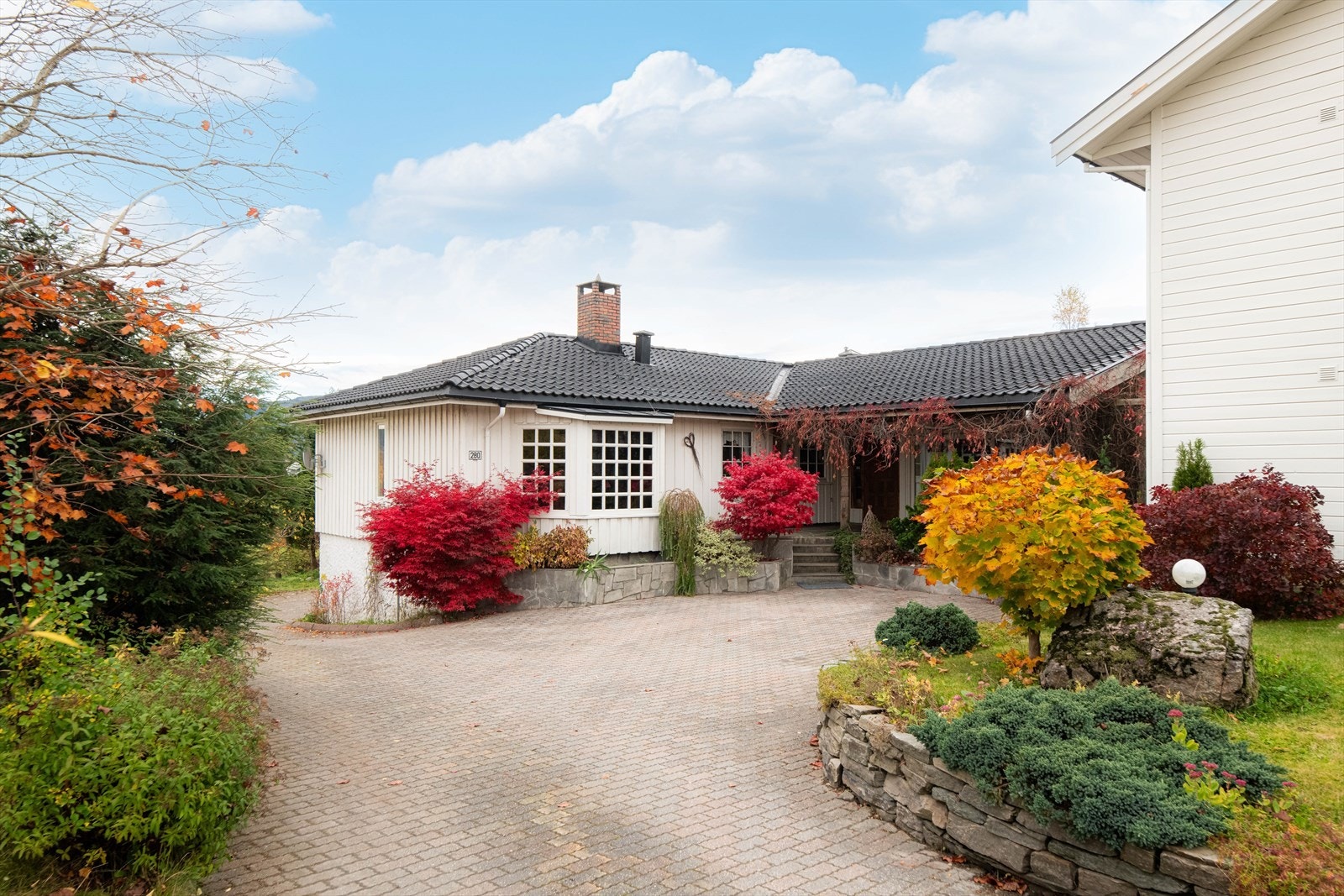 Tomten er pent opparbeidet med plen og flott beplantning, støttemurer og romslig gårdsplass med belegningsstein. Galleribilde