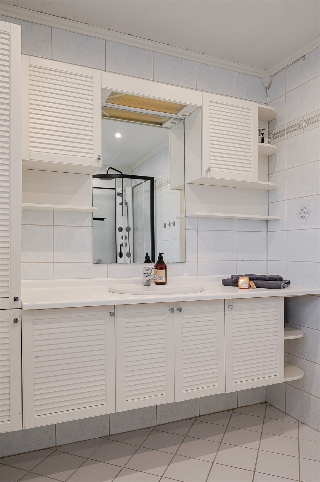 Lys og tidløs baderomsinnredning med rillede fronter og laminert benkeplate med nedfelt servant, speil med belysning og vegghengte skap over. Galleribilde