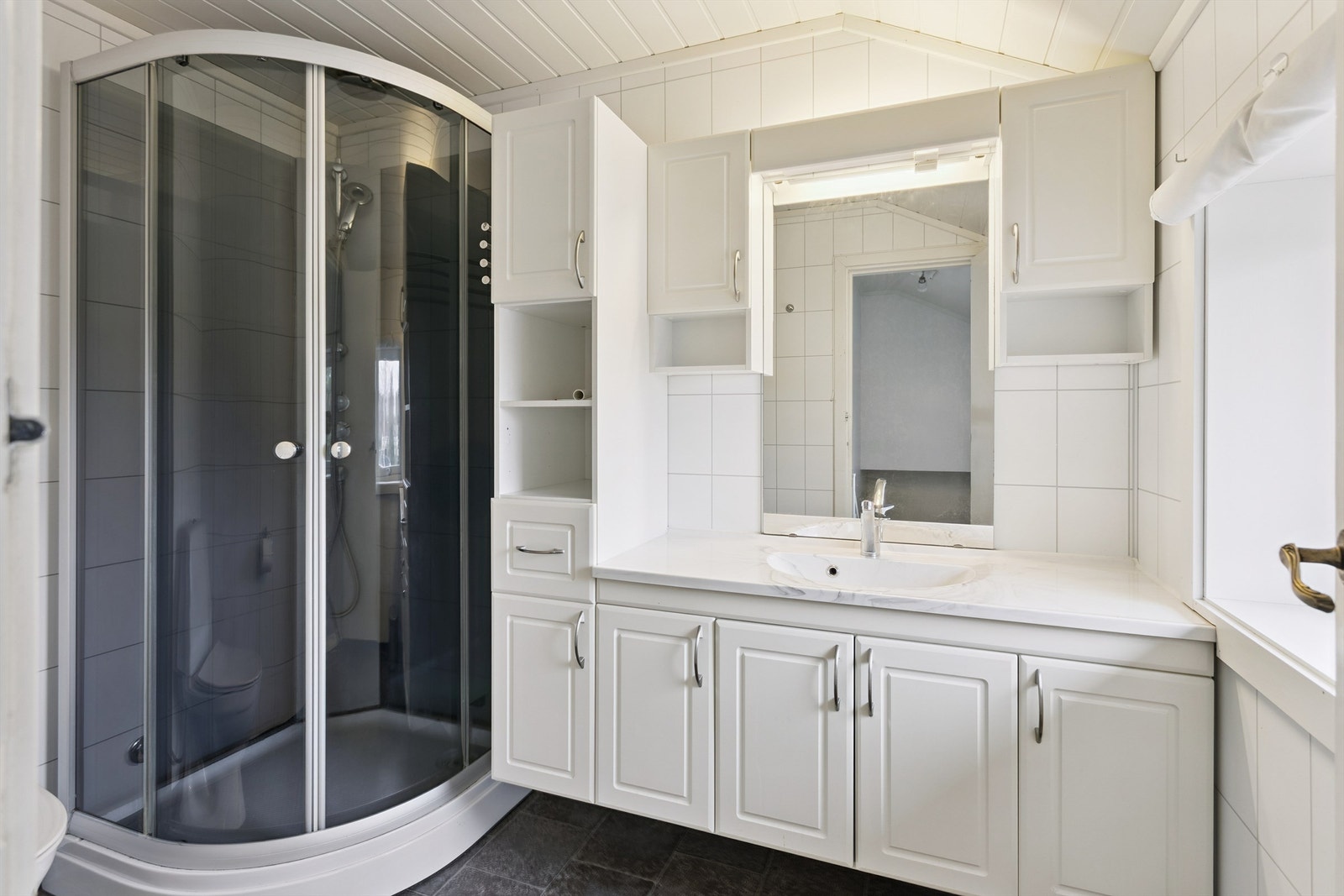 Badet er innredet med praktisk dusjkabinett som hindrer unødig vannsøl. Rikelig med oppbevaringsplass i baderomsinnredningen. Galleribilde